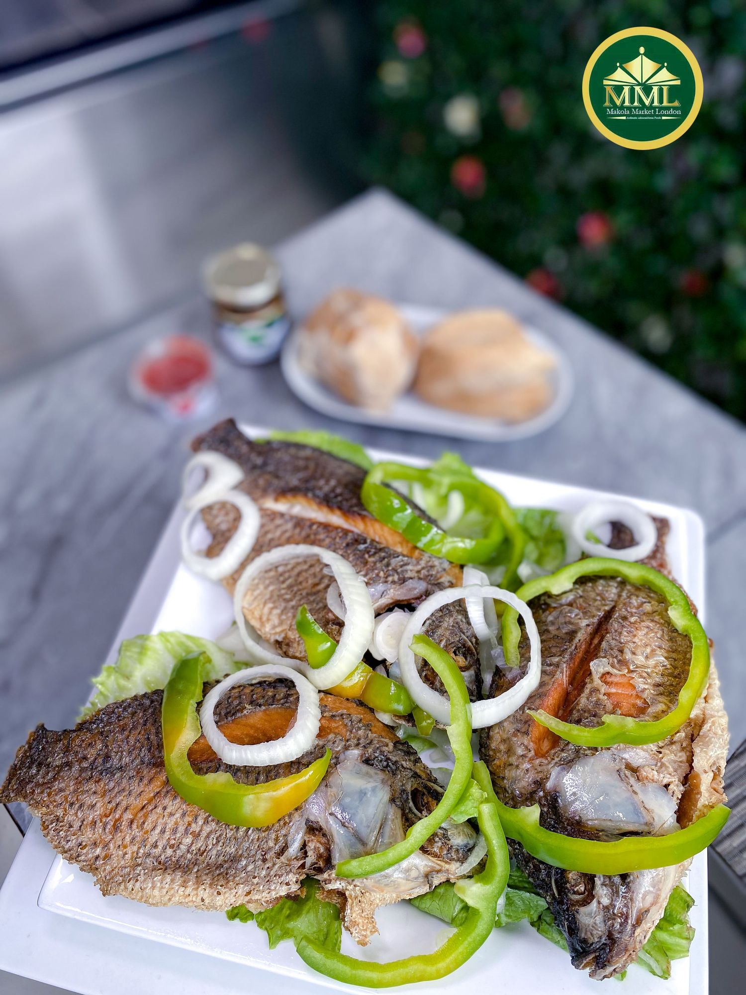 Grilled whole fish garnished with fresh onion rings, bell peppers and lettuce served on a white plate with rolls on the side.