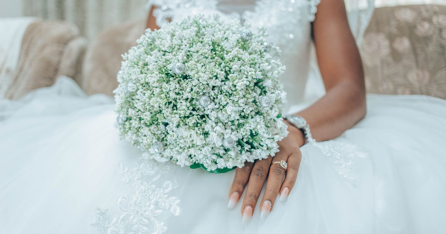 Close-up view of delicate baby's breath bouquet being held by hands wearing white lace gloves against a light background.