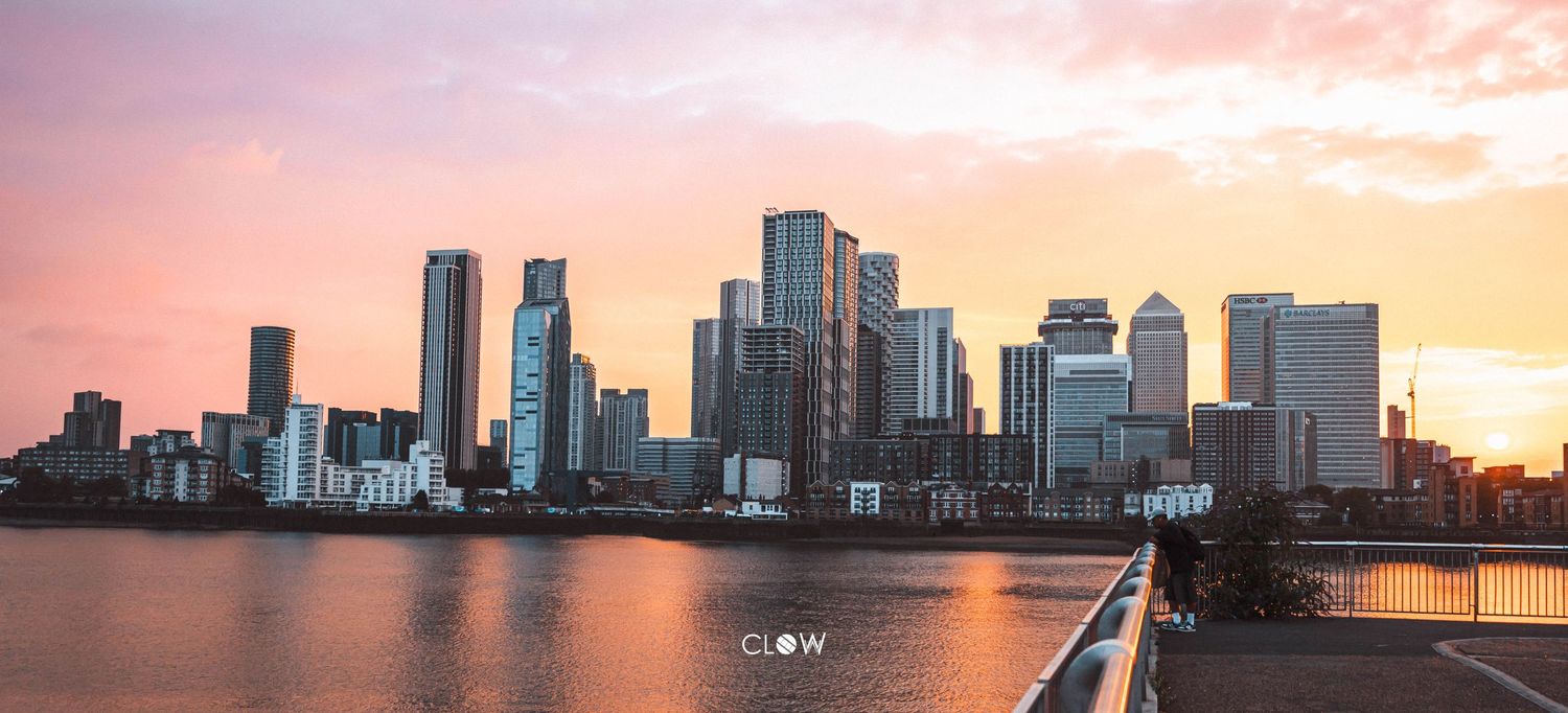 London's Canary Wharf skyline reflects in Thames River during golden sunset with modern skyscrapers illuminated.