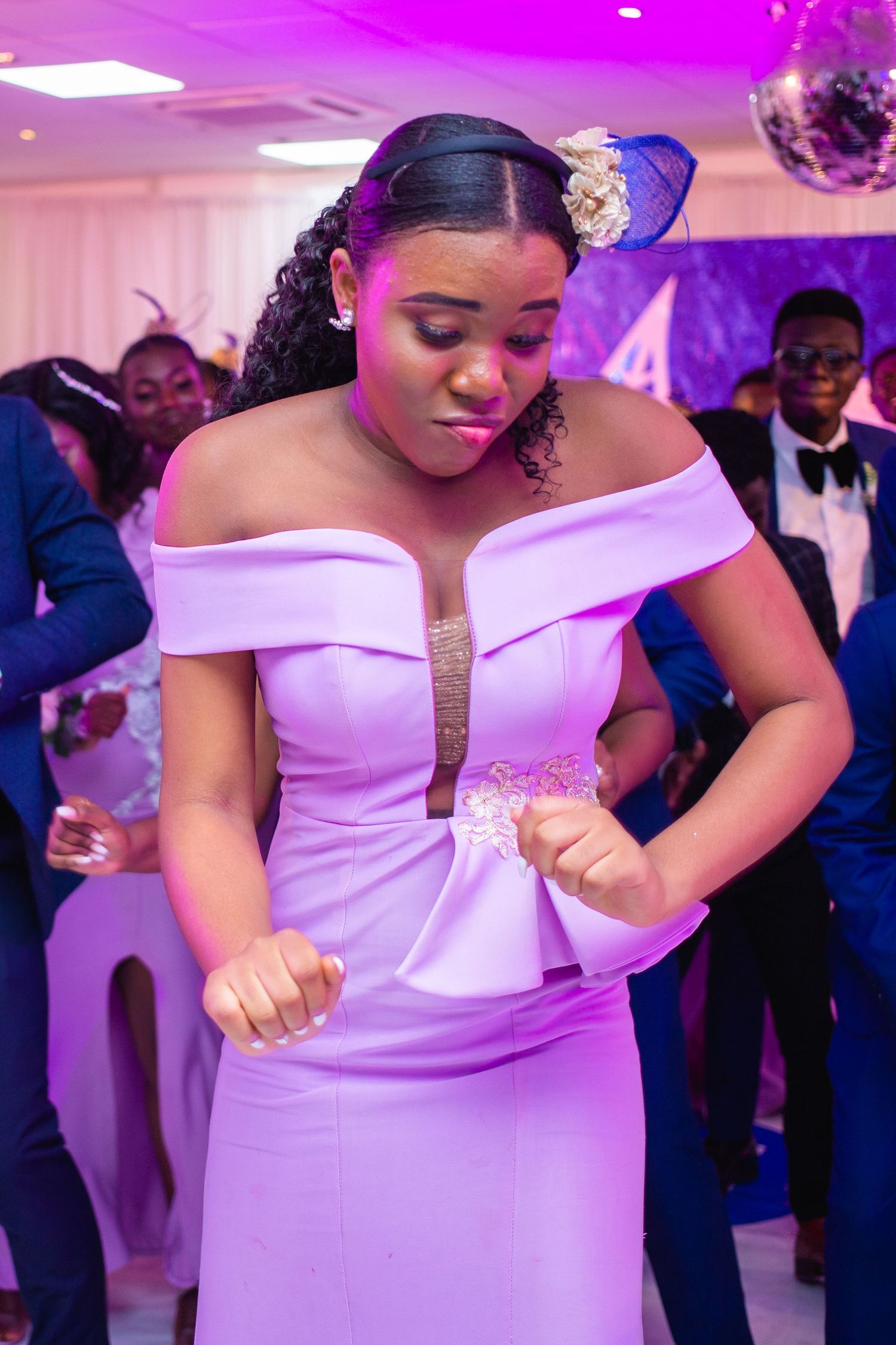 A group of wedding guests in navy blue suits dancing alongside someone in an elegant white off-shoulder gown at a reception.