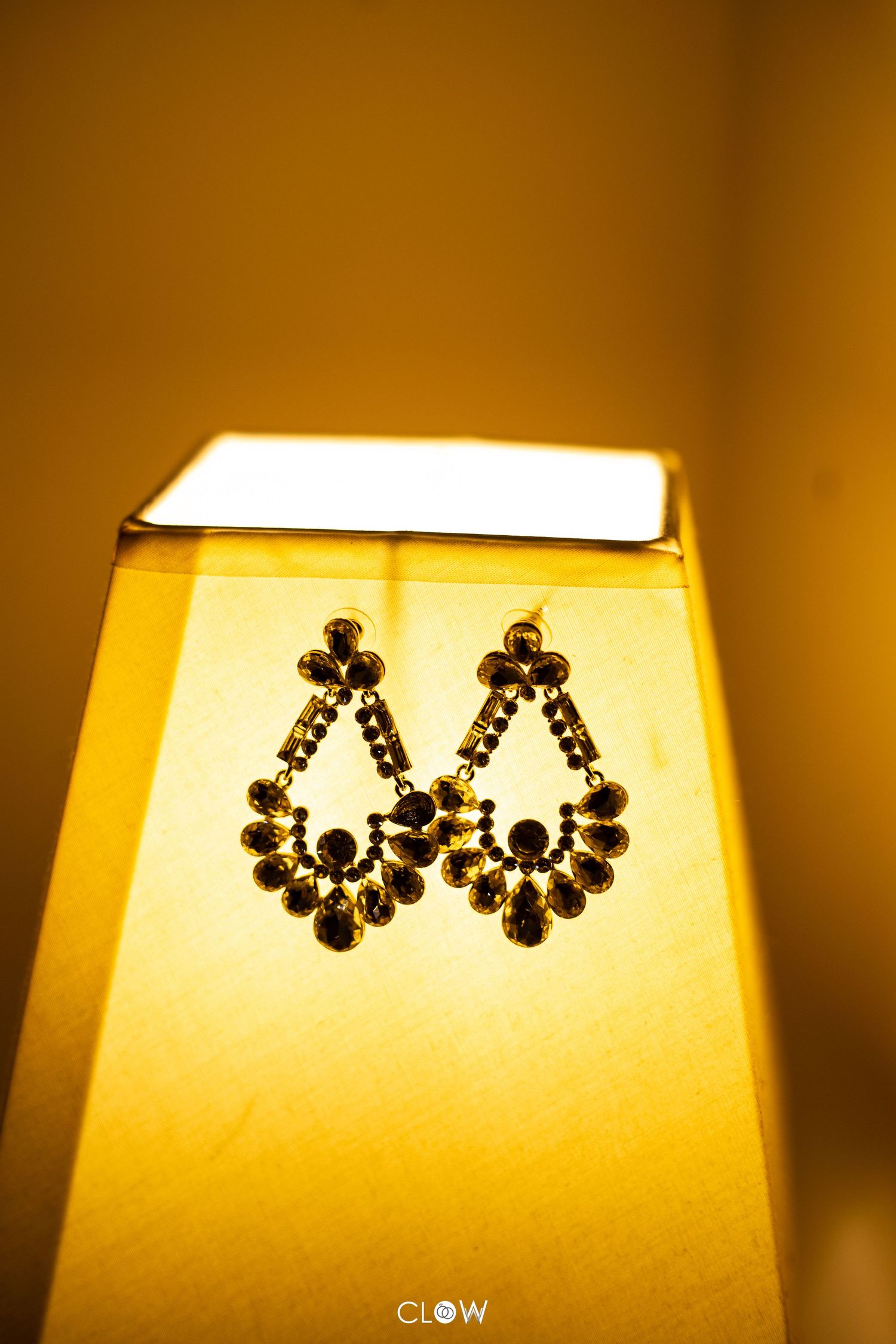 Elegant black crystal chandelier earrings photographed against warm yellow lamplight on a conical lampshade.