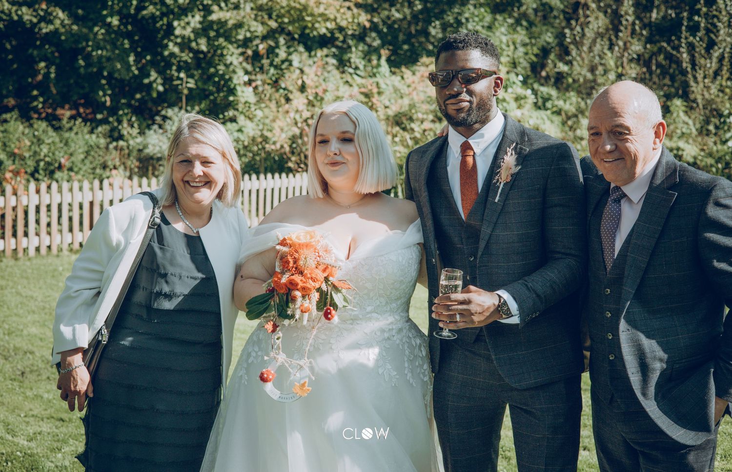 Group portrait at a garden wedding featuring people in formal attire and bouquets on a sunny day.