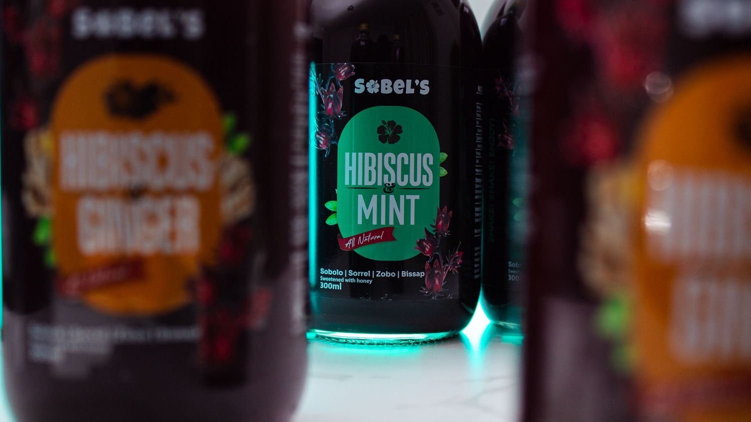 Three bottles of Hibiscus Mint and ginger beverages displayed with dramatic lighting.
