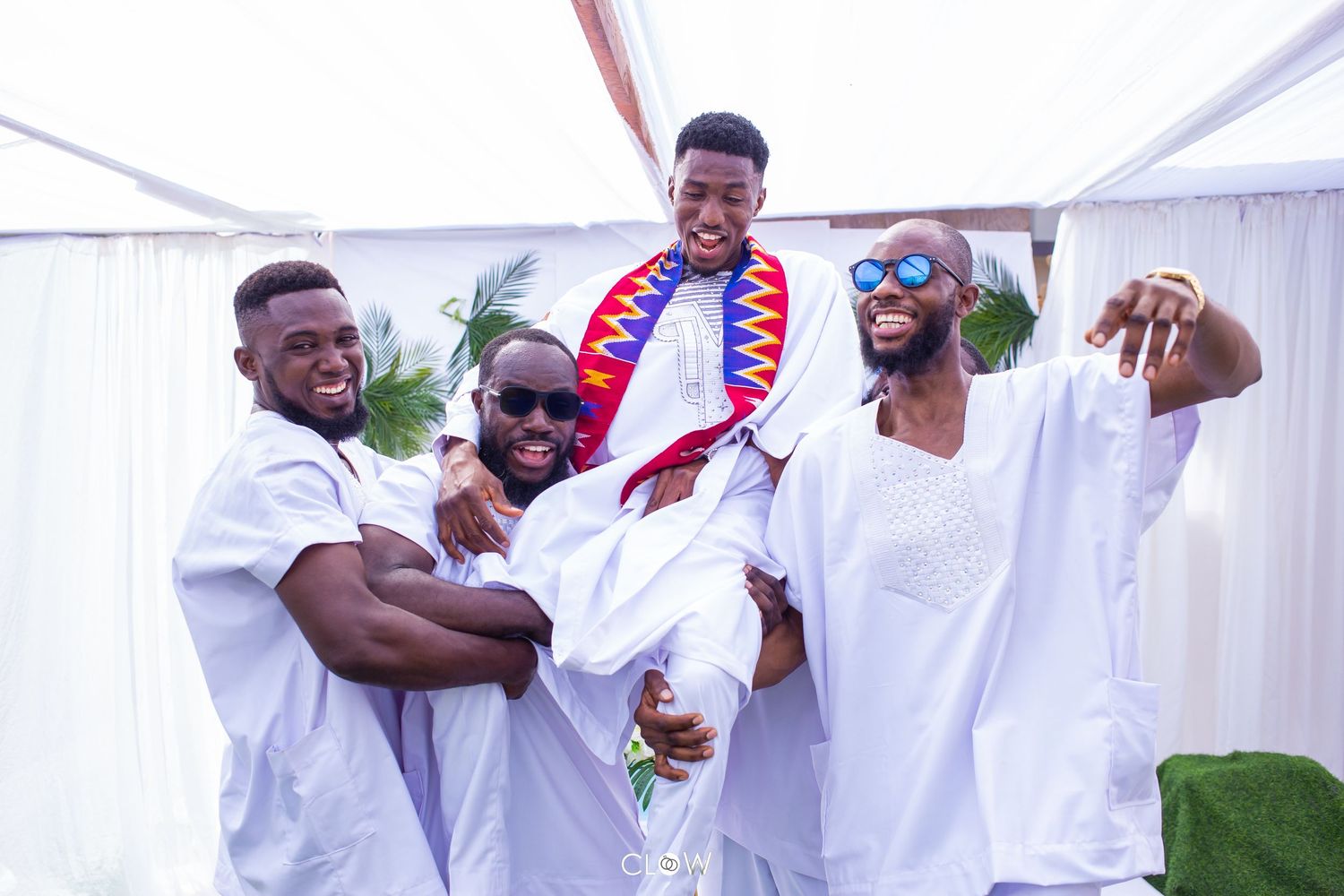 A group of people in white outfits dance joyfully at what appears to be a wedding celebration or party.