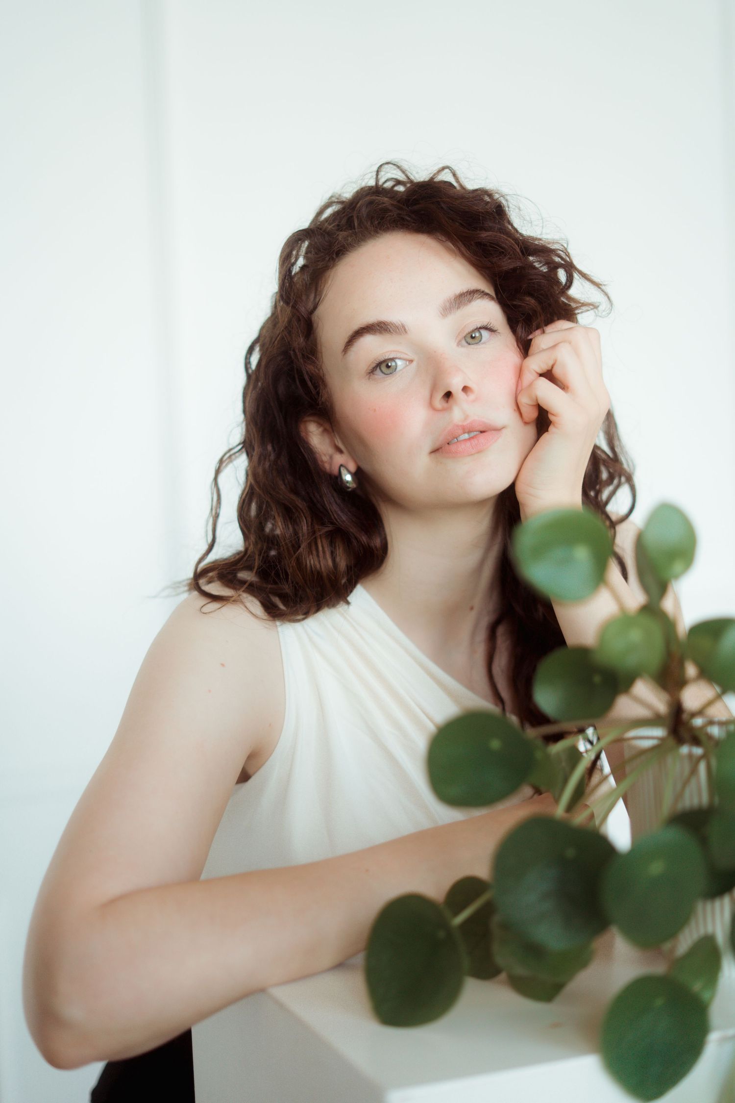 Fair skinned female Model with reddish Brown curls and a pilea plant