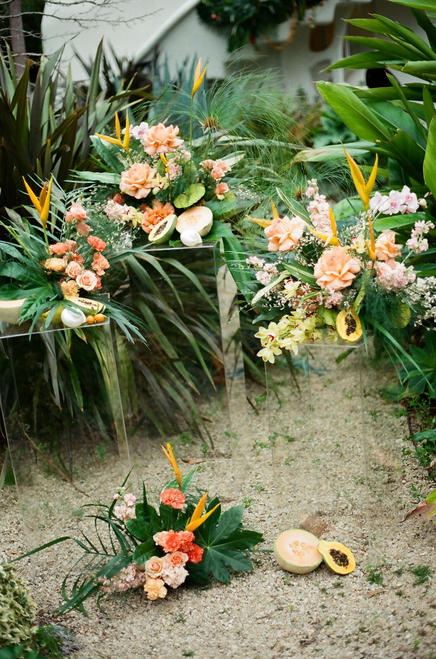 Lush tropical wedding floral arrangements with peach roses and birds of paradise on sandy ground.
