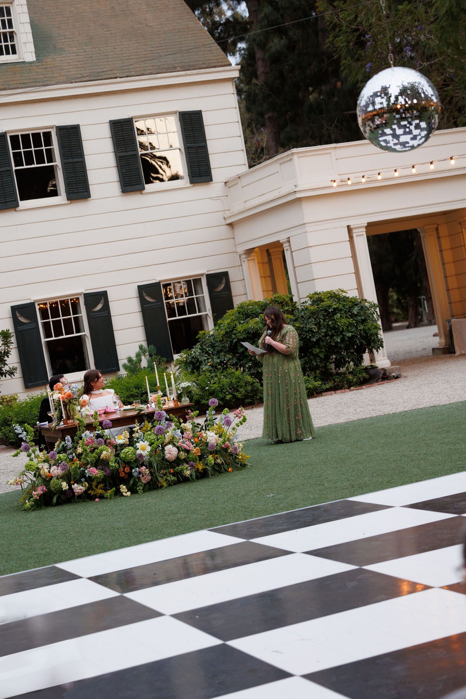 Aerial view of outdoor wedding reception with checkered dance floor, floral sweetheart table, and elegant white venue.