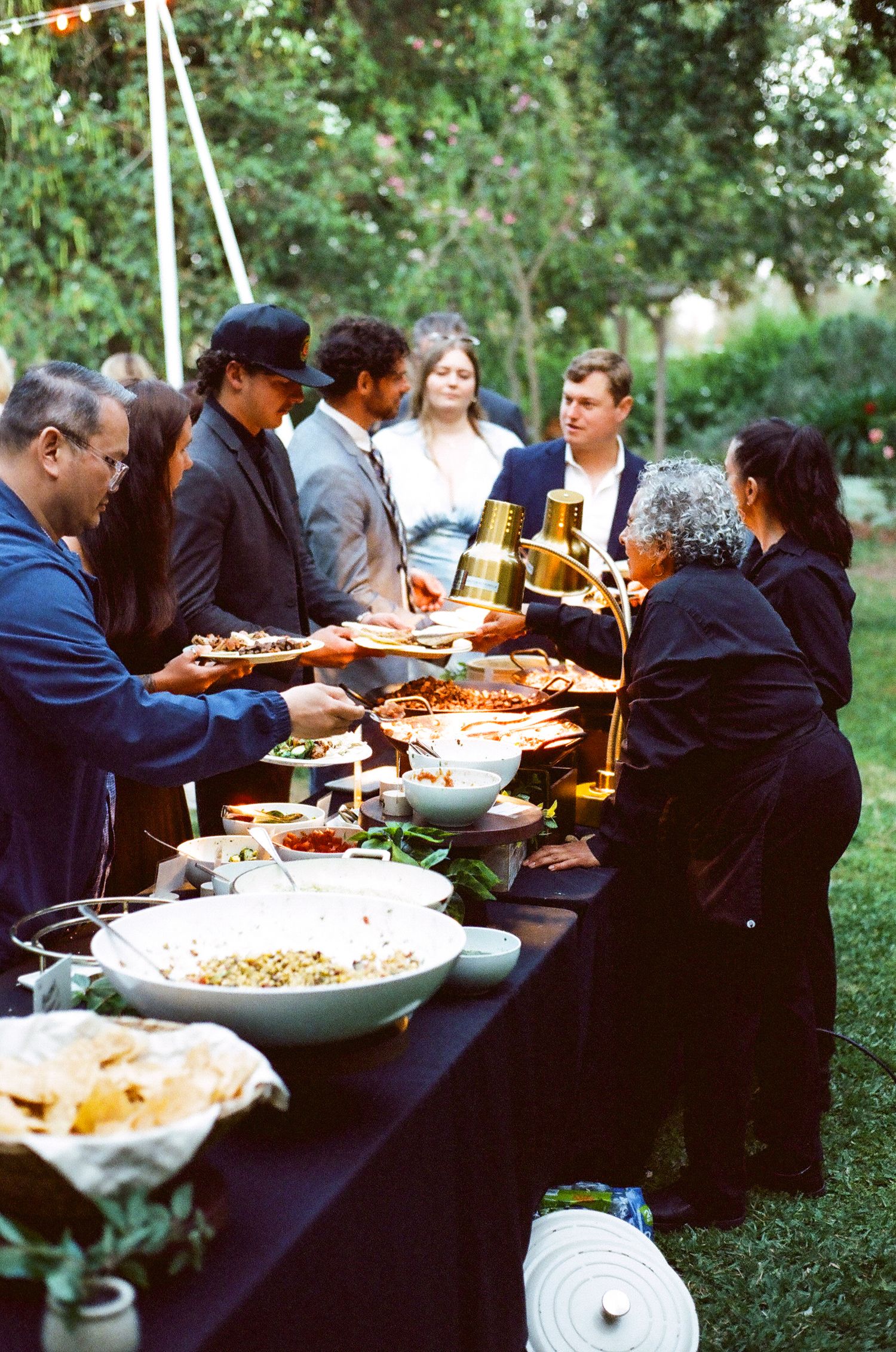 Guests serving themselves at an elegant outdoor buffet table during a garden party event.