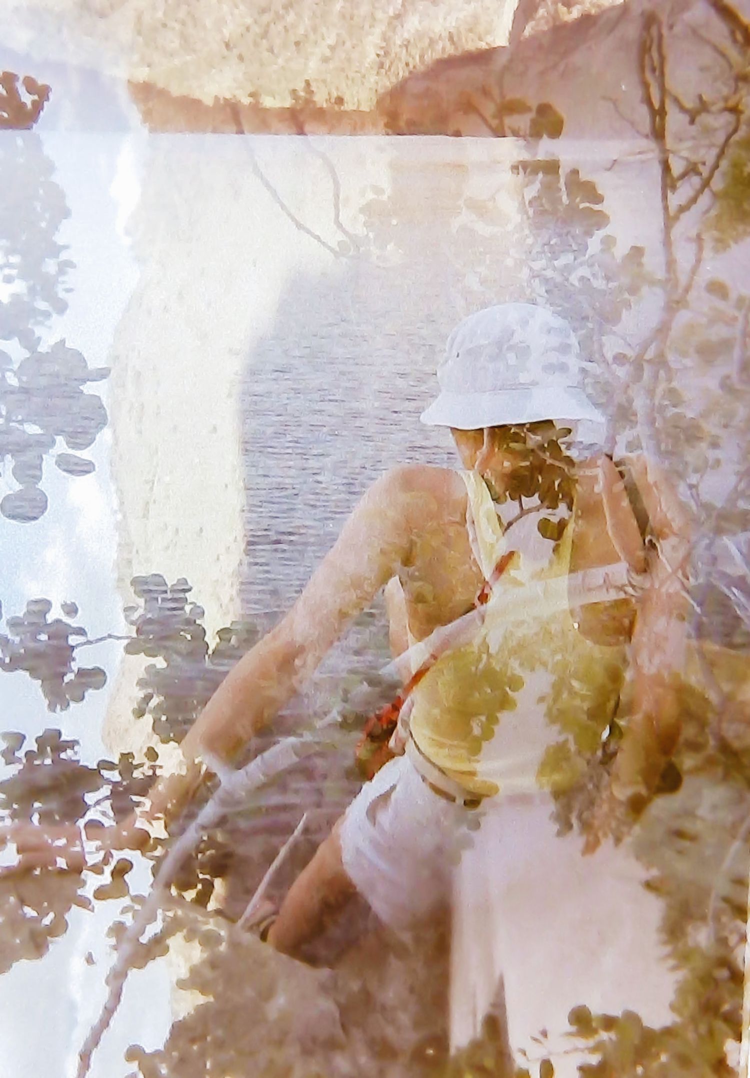 Double exposure photo of a woman in white sitting near a serene lake surrounded by trees.