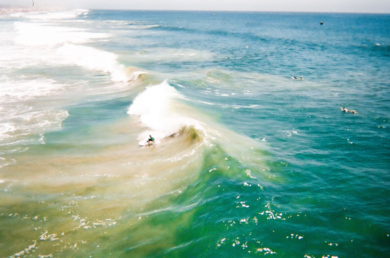 Aerial view of surfer riding a large curling ocean wave in turquoise water.