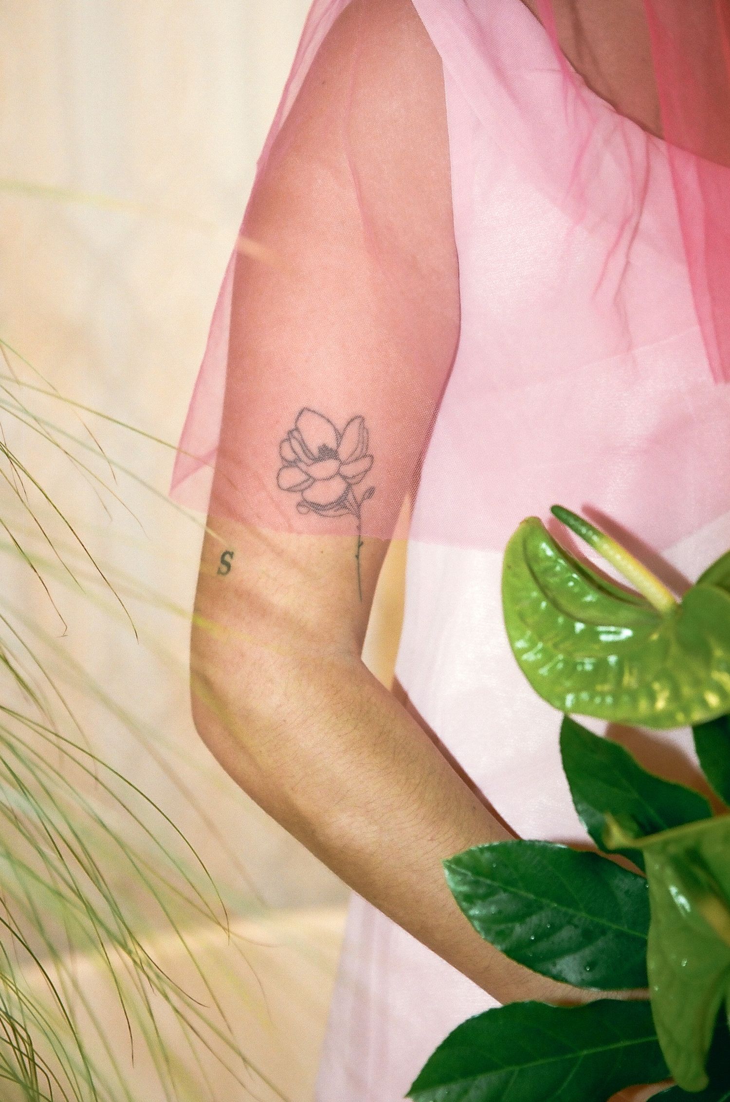 Close-up of a small flower tattoo on a woman's arm wearing a sheer pink dress.