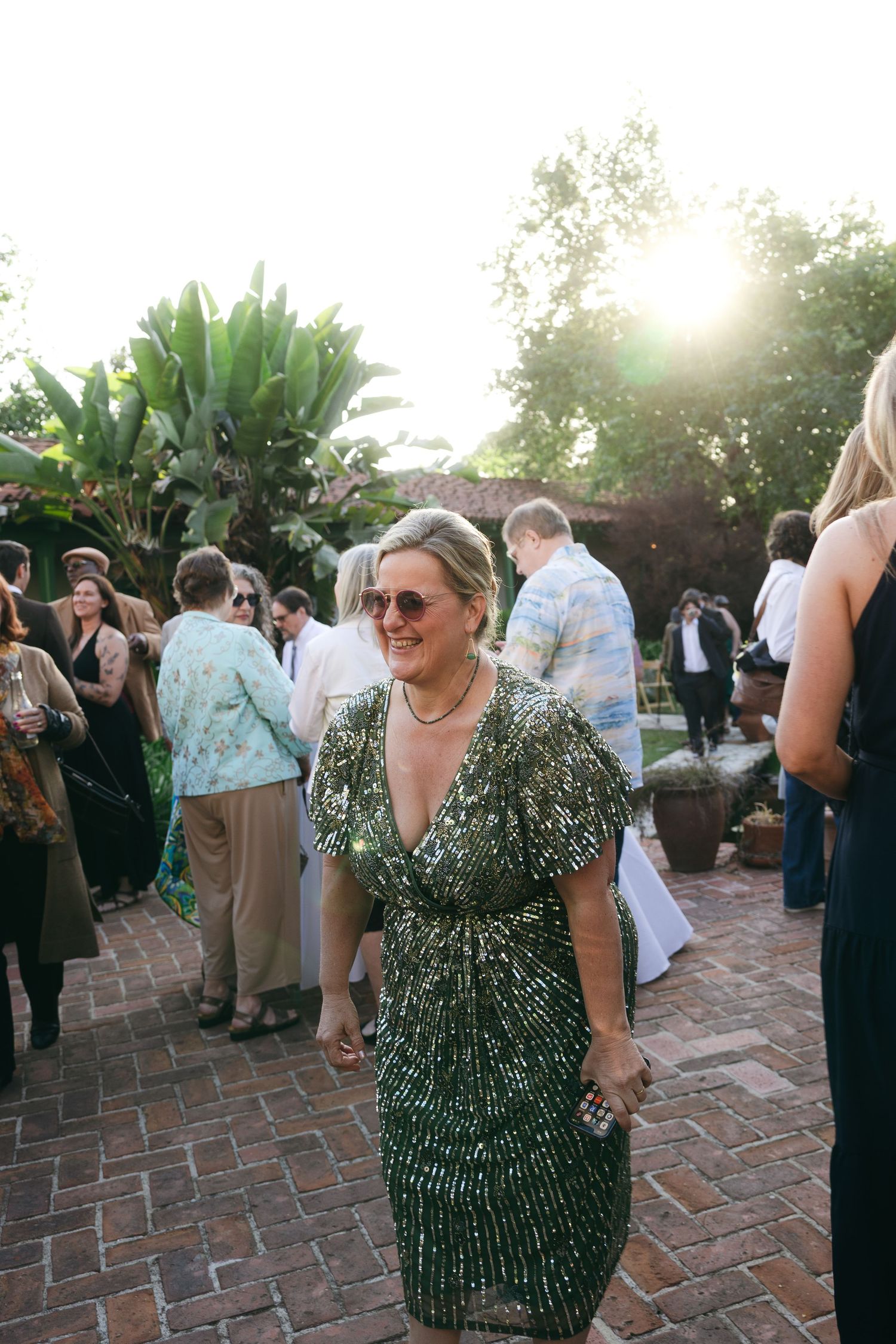 Woman in green sequin dress smiling at outdoor garden party event during golden hour sunset.