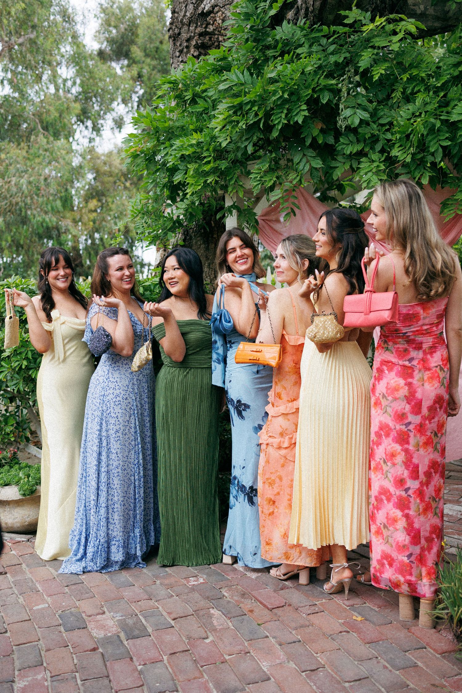 Group of eight women in colorful maxi dresses posing and laughing at an outdoor wedding.