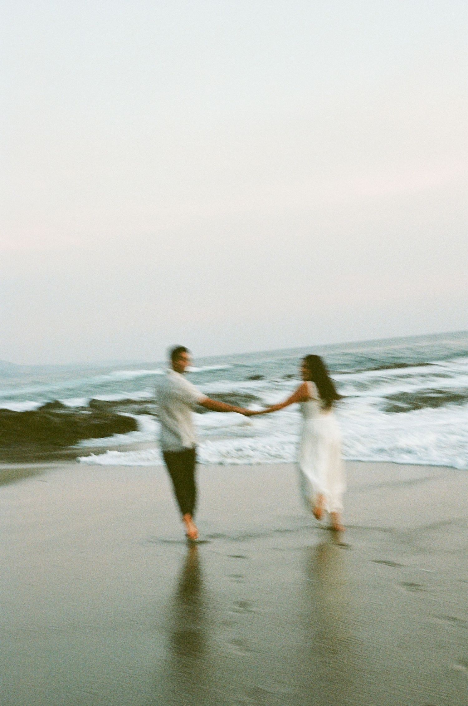 Couple holding hands and dancing on a sandy beach at dusk.