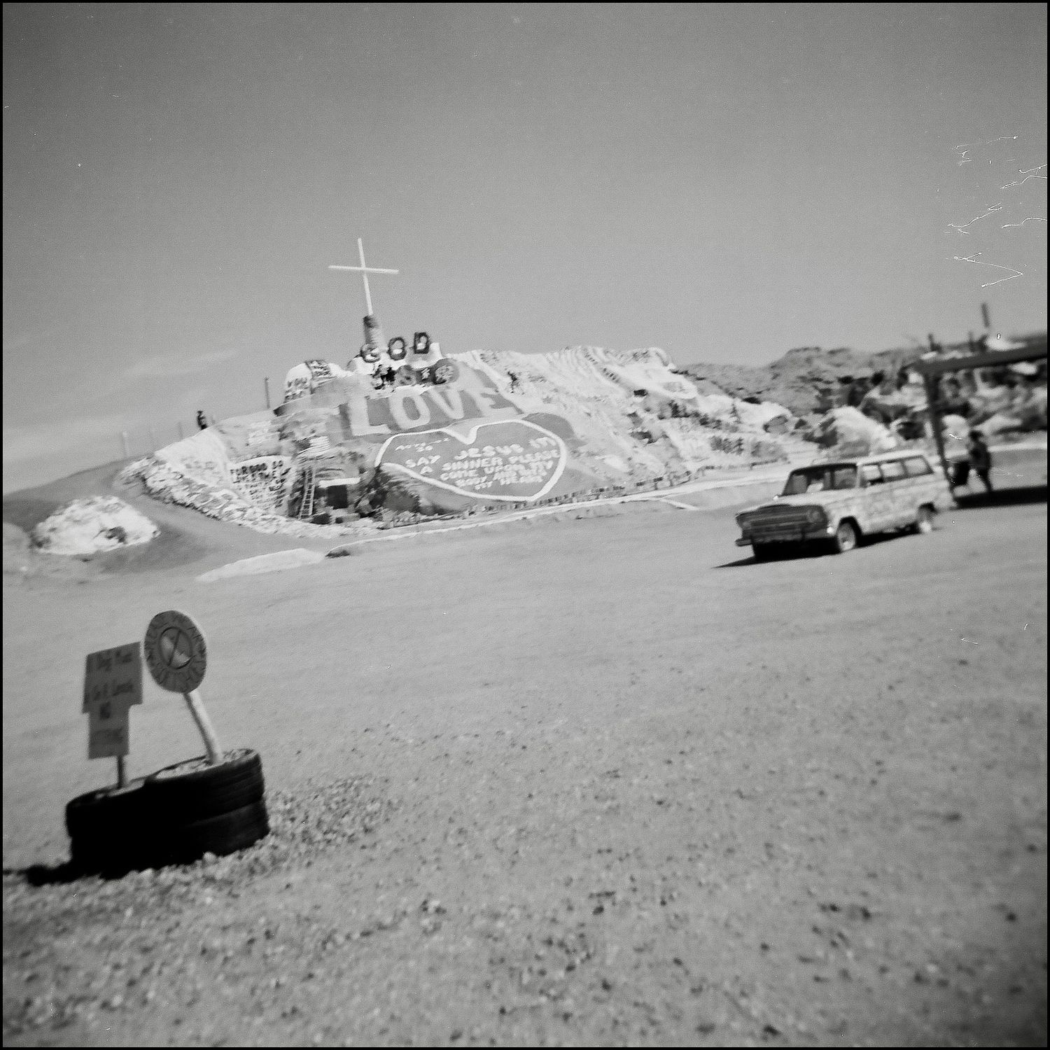 Black and white photo of desert roadside rock painted with God is Love and a cross.