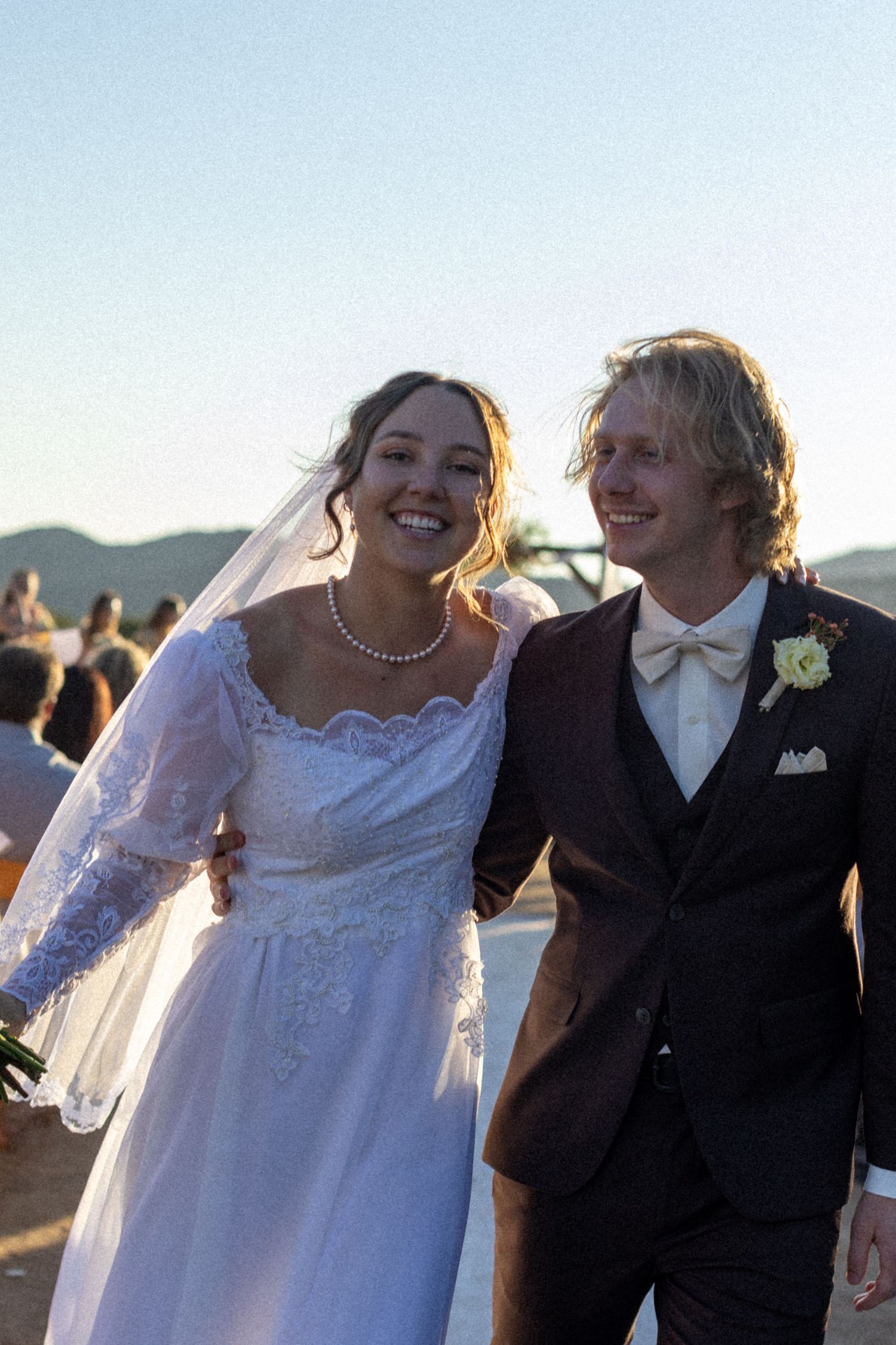 Happy bride and groom walking together outdoors at golden hour after their wedding ceremony.