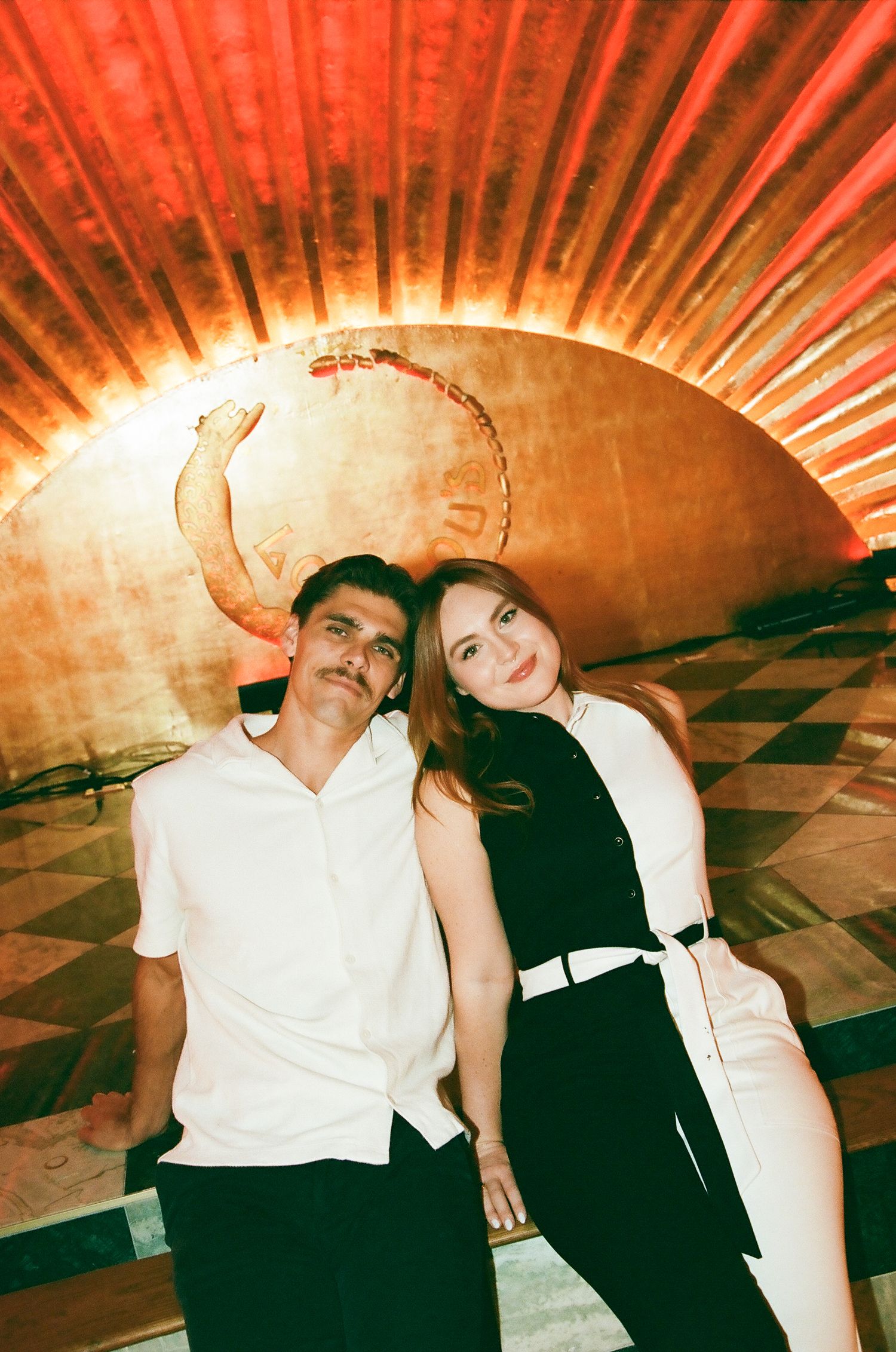 Couple posing together under a dramatic red glowing circular ceiling in a warmly lit interior.