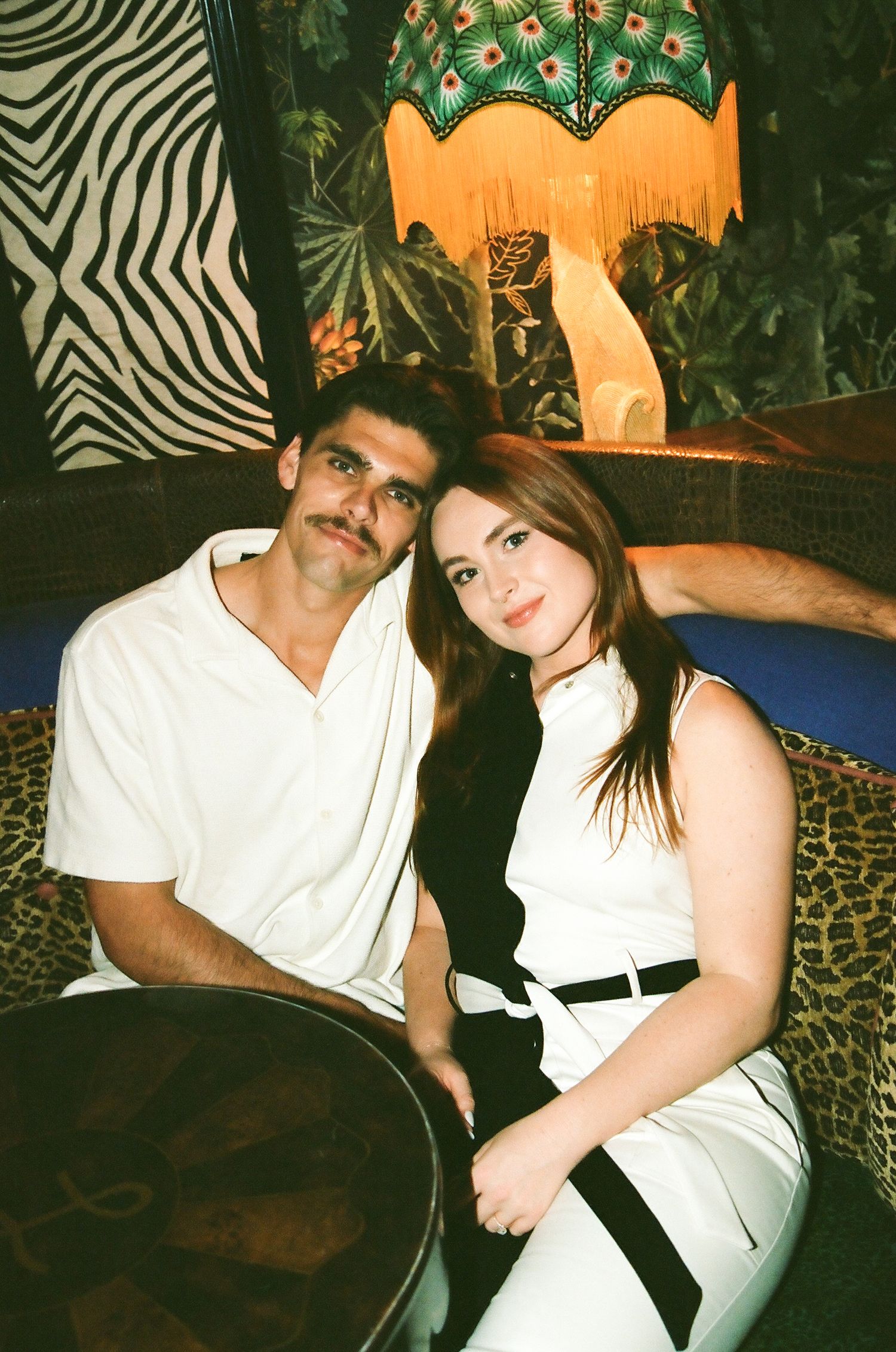 Couple sitting together in a vibrant, eclectic lounge with zebra print and tropical decor.