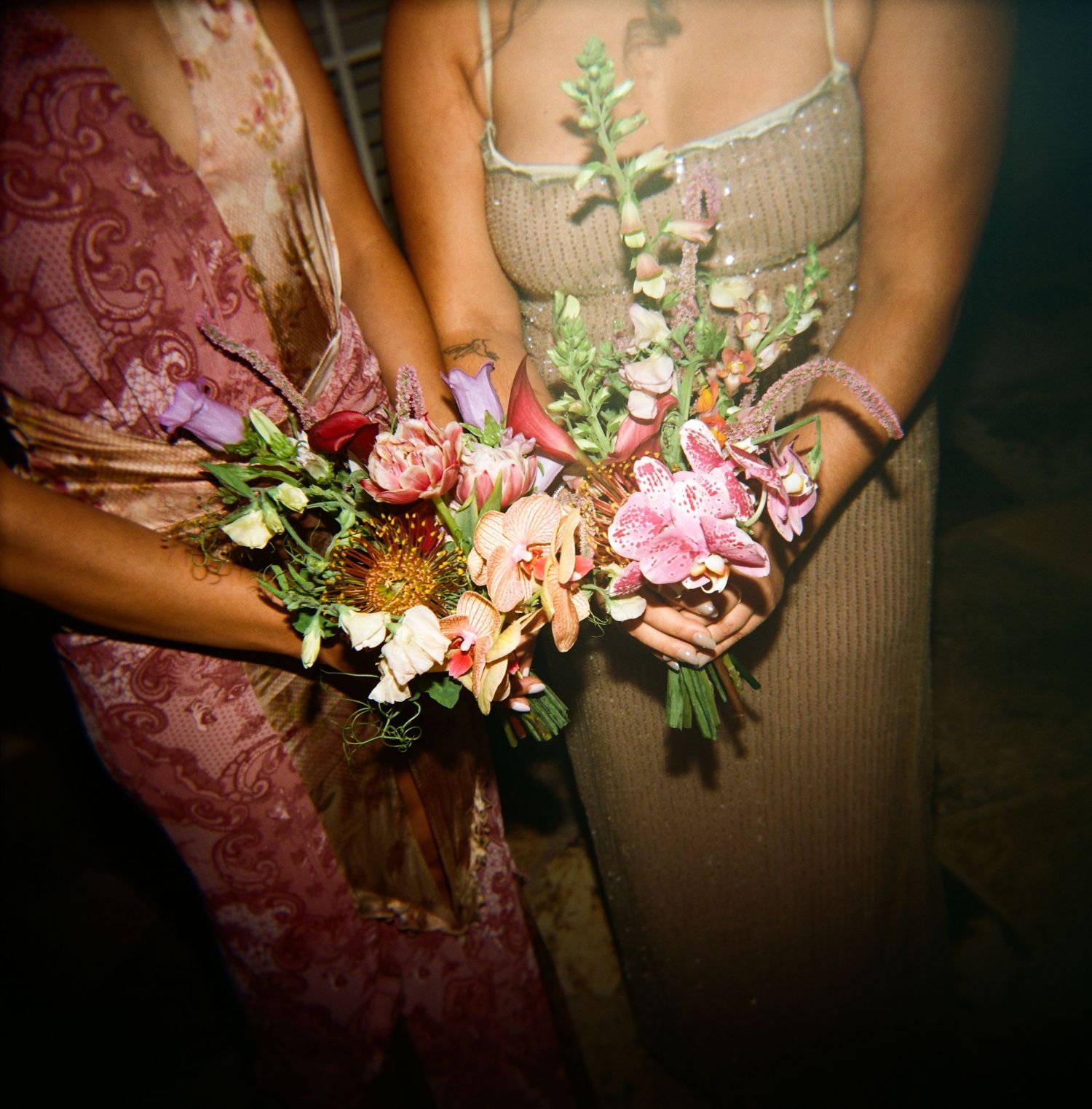 Two bridesmaids holding colorful pink and orange floral bouquets at outdoor wedding reception.
