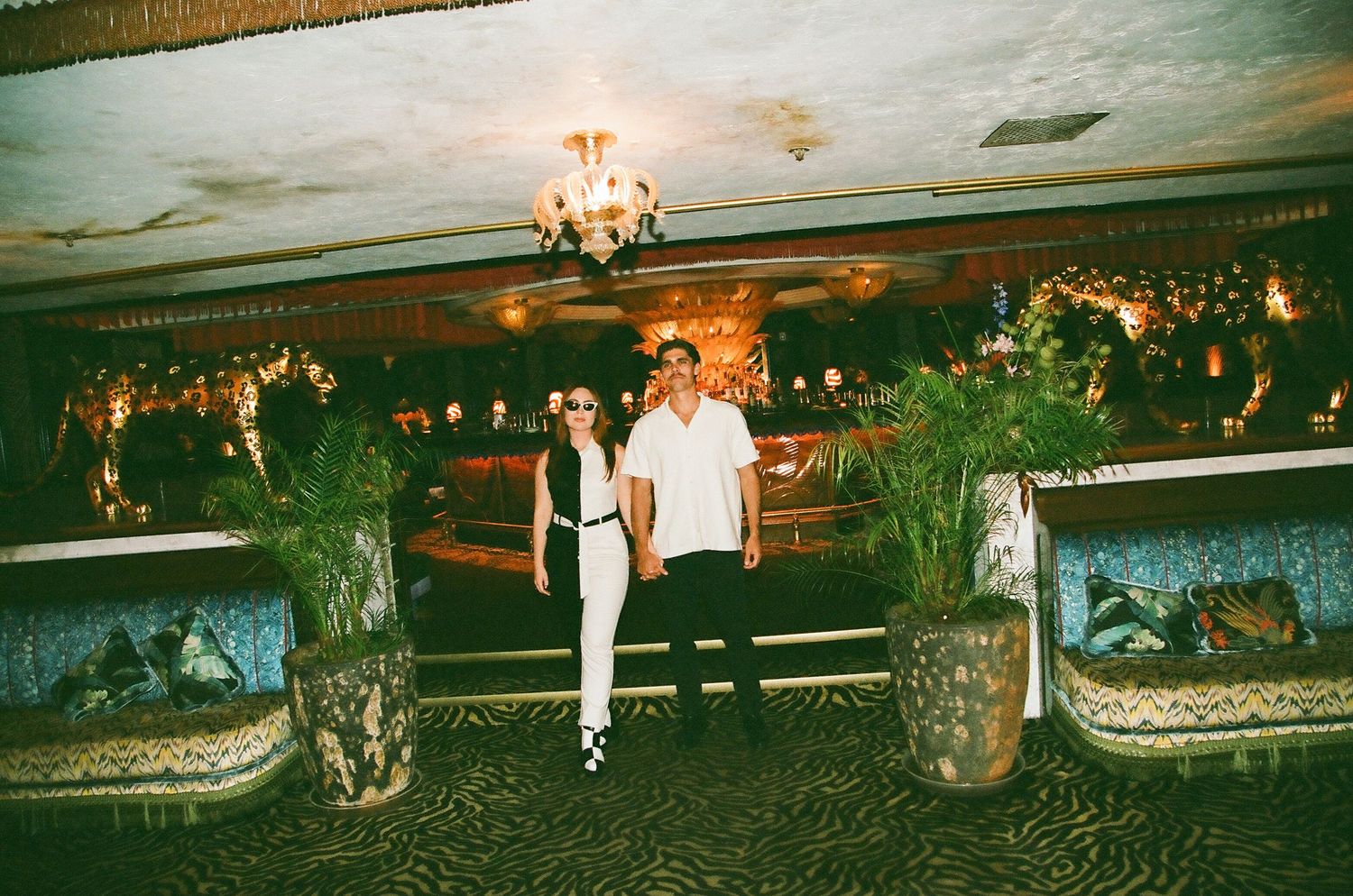 Couple standing together in ornate decorated indoor venue with tropical plant decor.