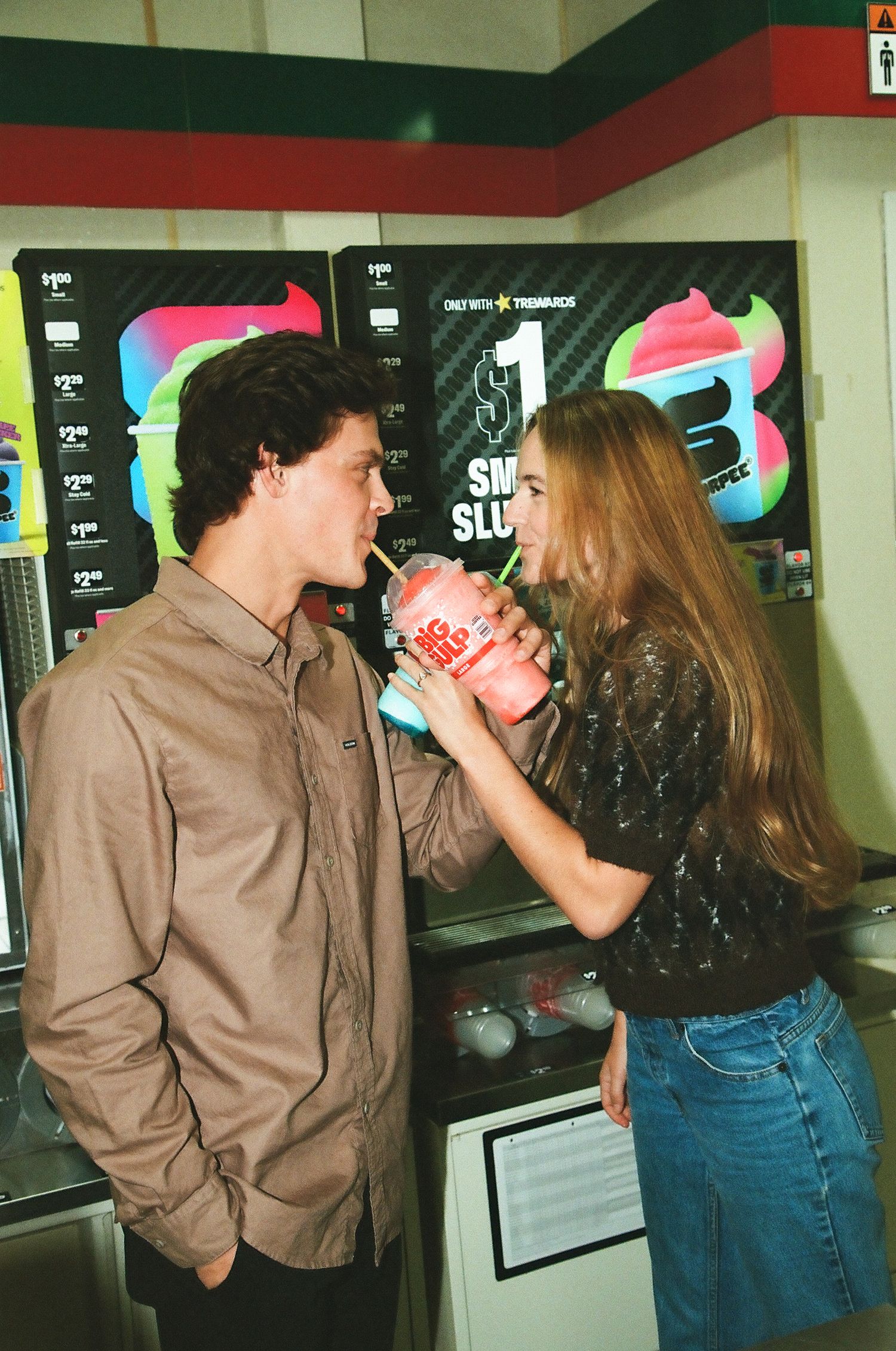 Young couple sharing a Slurpee drink together inside a 7-Eleven convenience store.