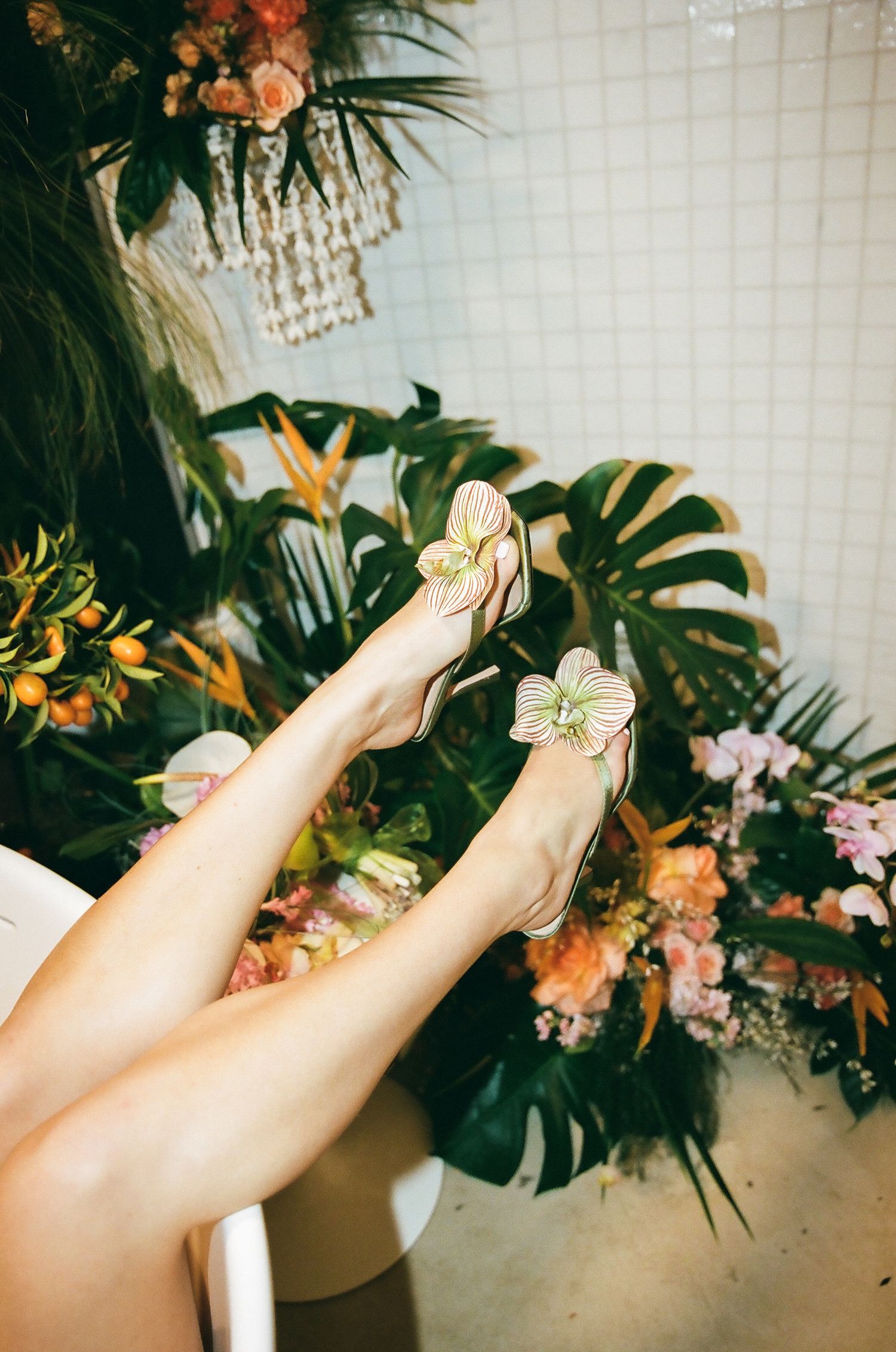 Elegant floral heels with orchid embellishment displayed against a backdrop of tropical greenery.
