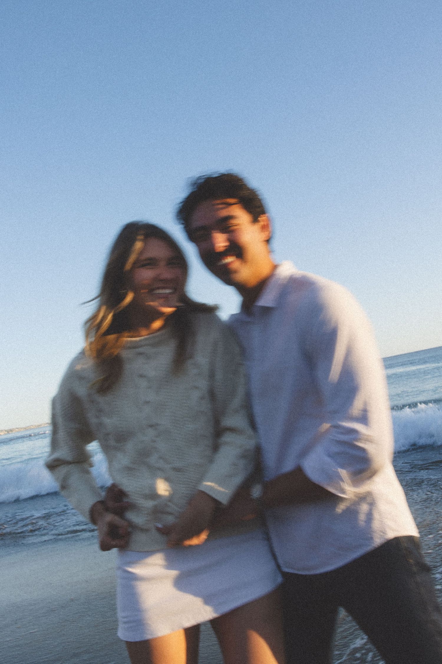 Blurred motion shot of smiling couple walking hand in hand on beach at golden hour.