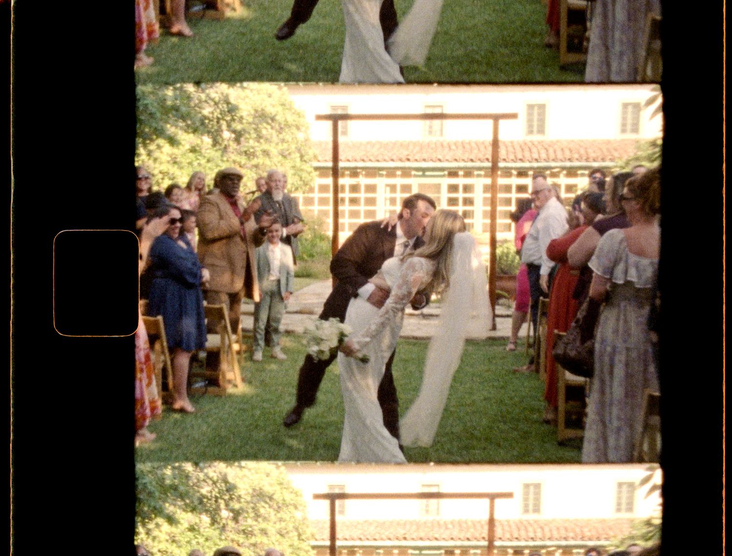 Outdoor wedding ceremony with couple sharing a romantic dip kiss at the altar, surrounded by guests on a sunny day.