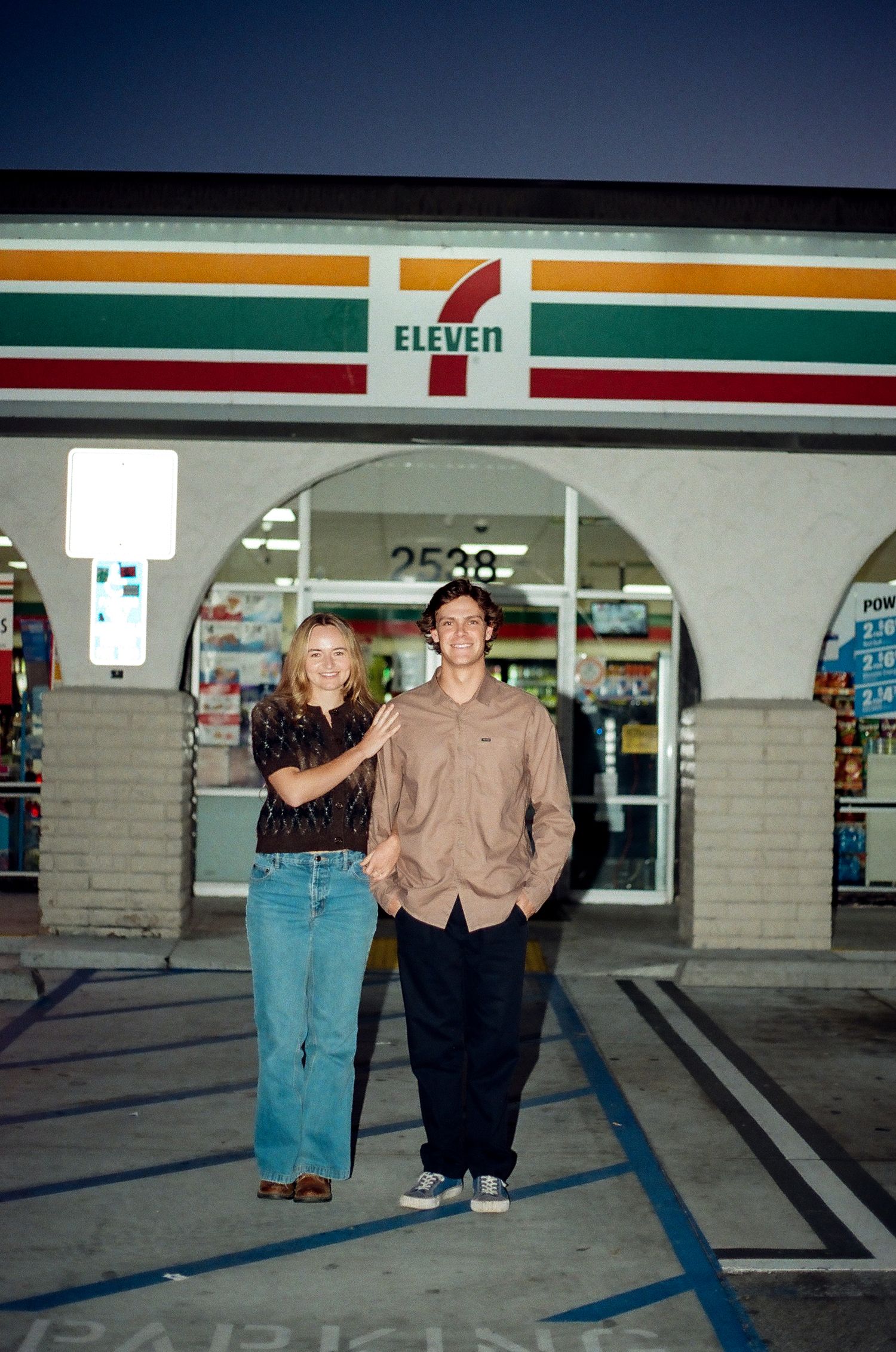 Couple smiling together outside a 7-Eleven store at night.