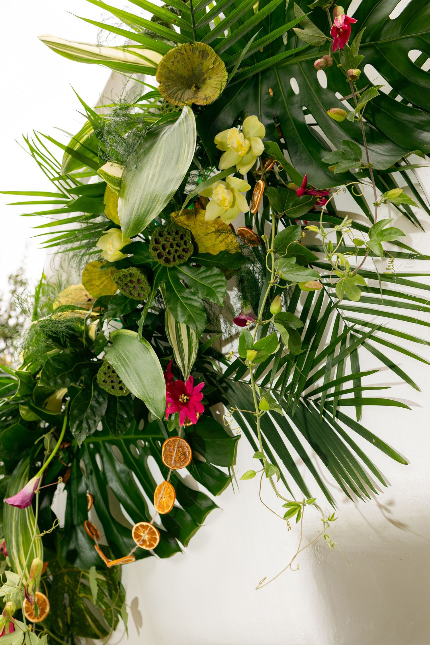 Lush tropical wedding arch with monstera leaves, orchids, lotus pods, and dried citrus slices.