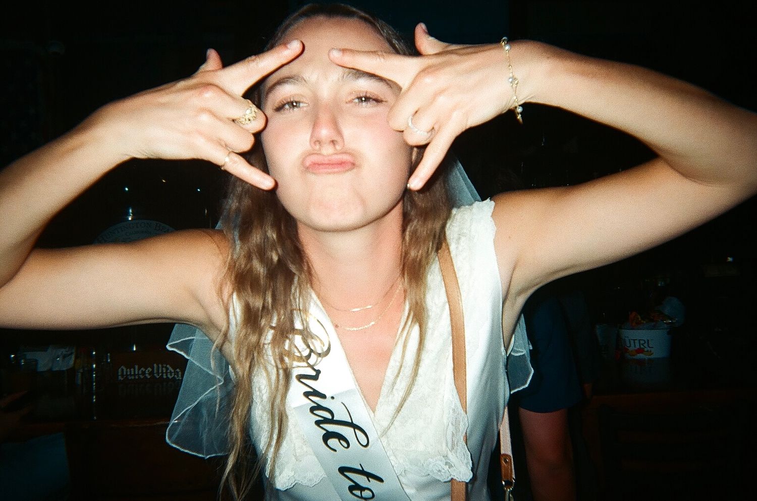 Young woman wearing a bride-to-be sash and veil making a funny face at a bachelorette party.