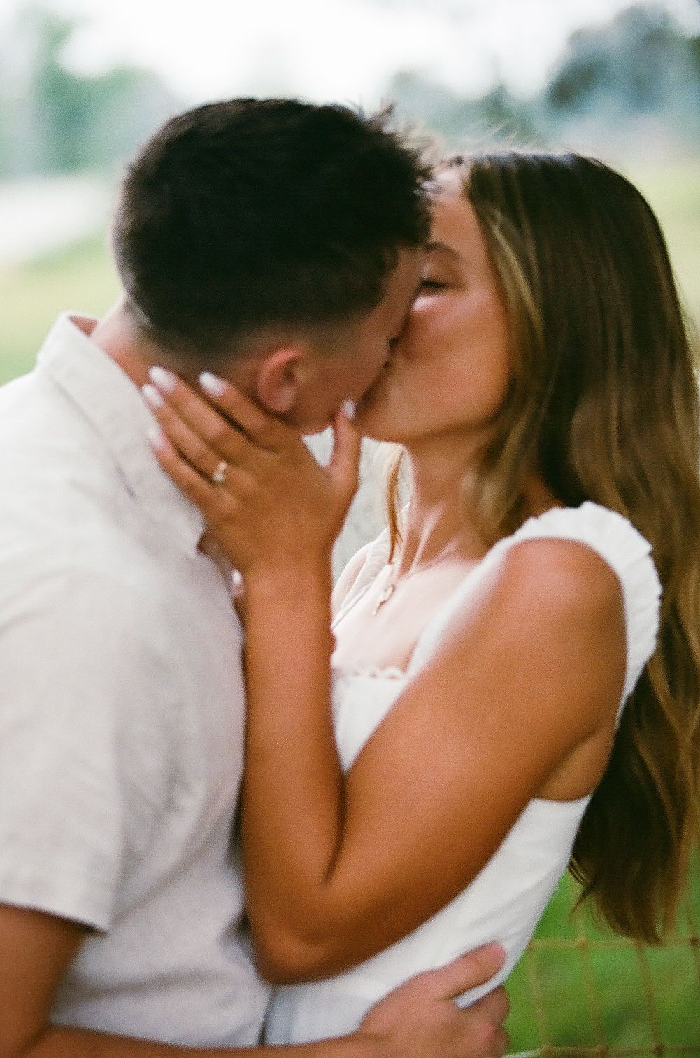 Couple sharing a romantic kiss outdoors during engagement photo session on film.