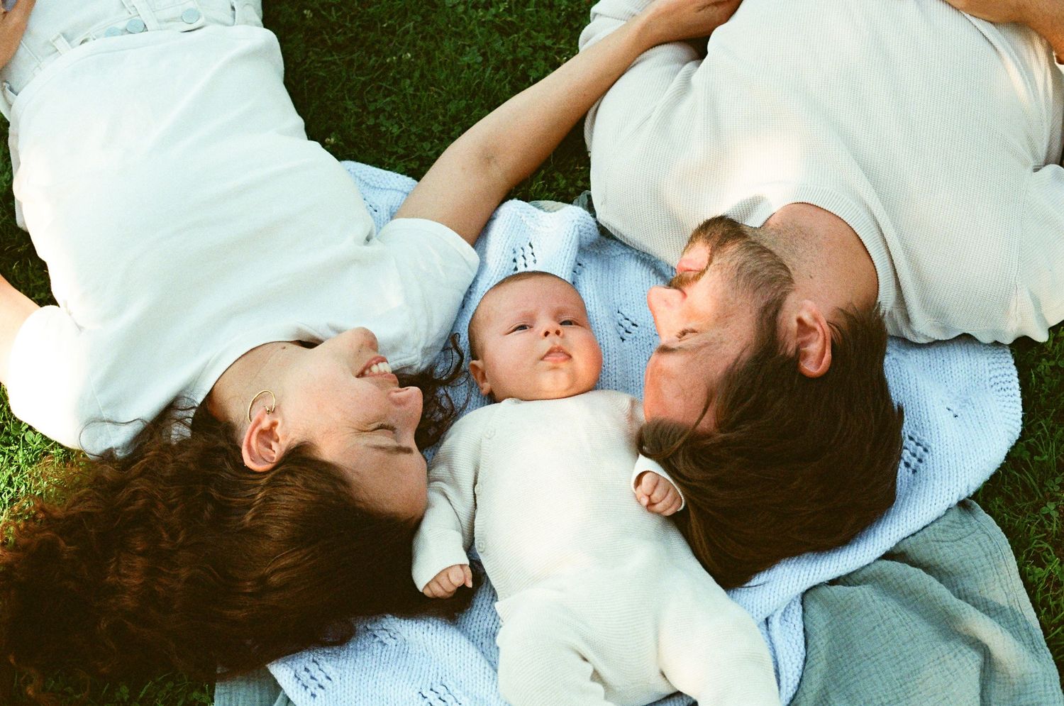 Aerial view of parents lying on grass with newborn baby between them.