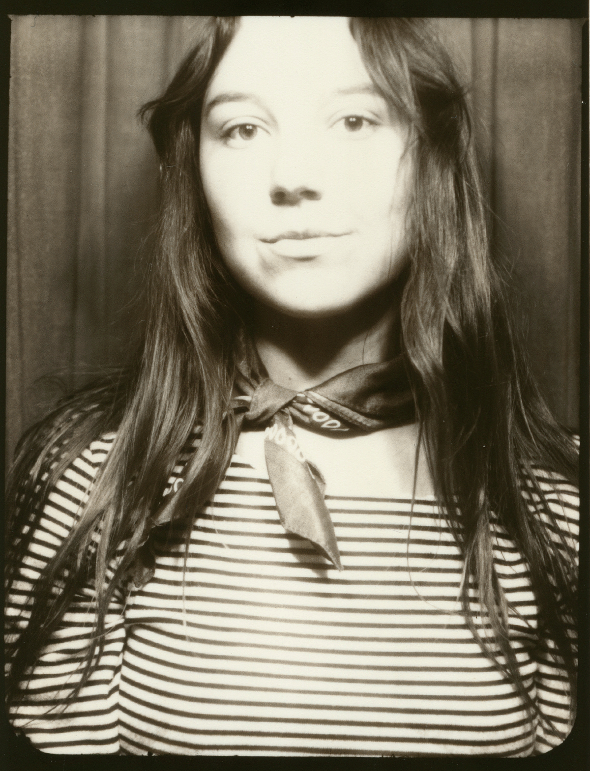 Black and white photo booth portrait of a young woman with long hair wearing a striped shirt and neck scarf.