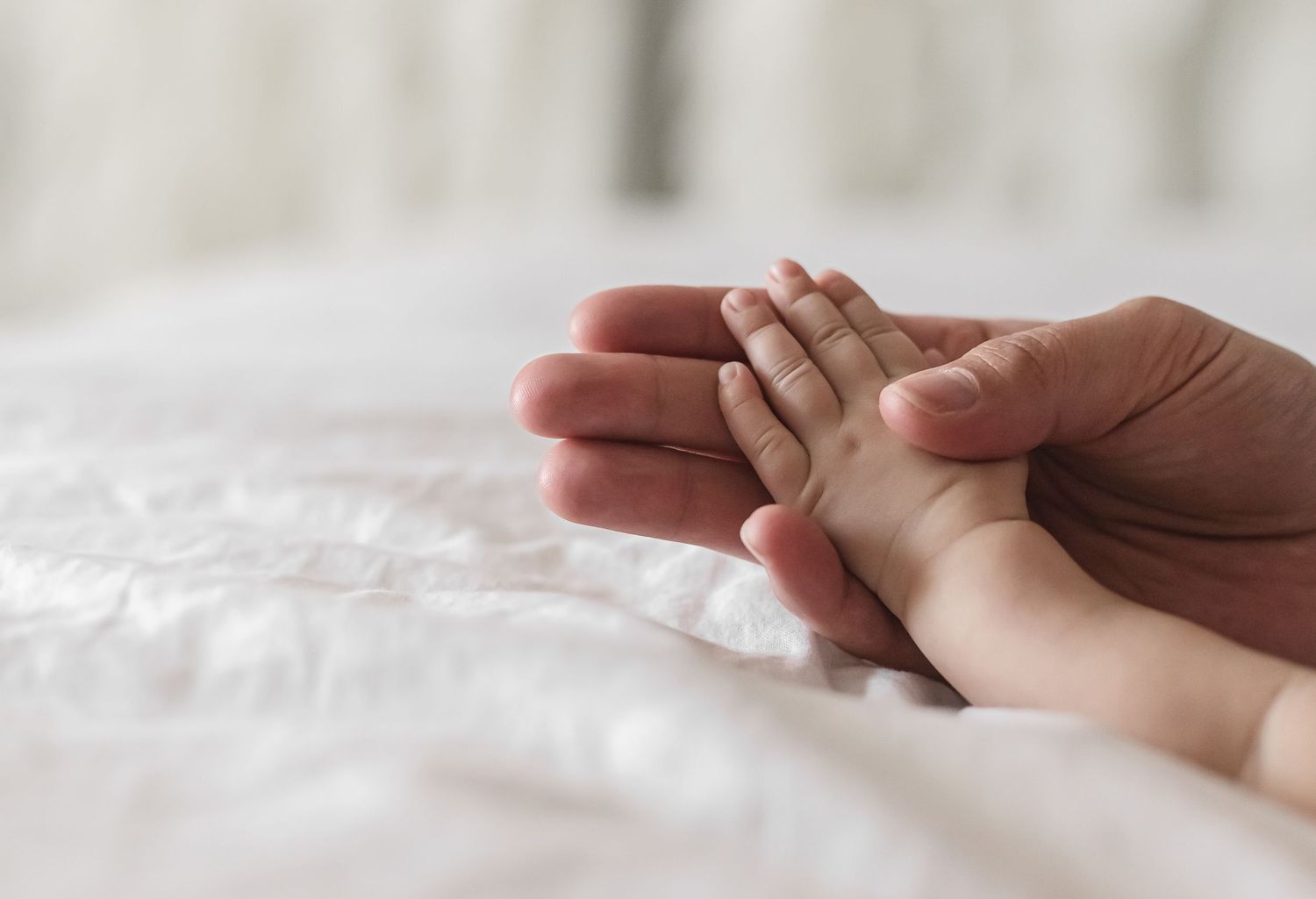 Close-up view of someone gently holding newborn baby hand