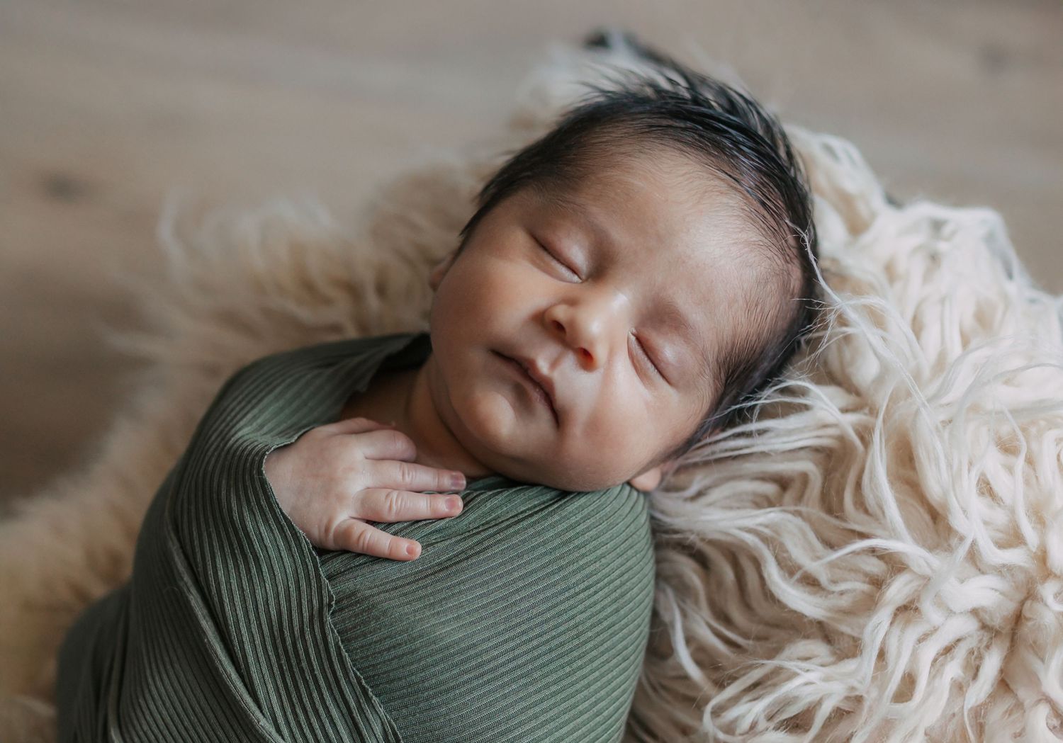 Sleeping newborn baby wrapped in green ribbed swaddle blanket rests peacefully on cream textured fabric.