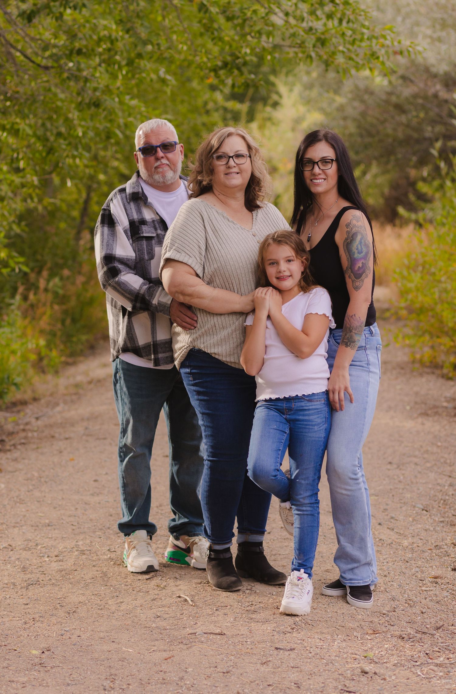 A family group poses on a dirt trail surrounded by green foliage on a sunny day.