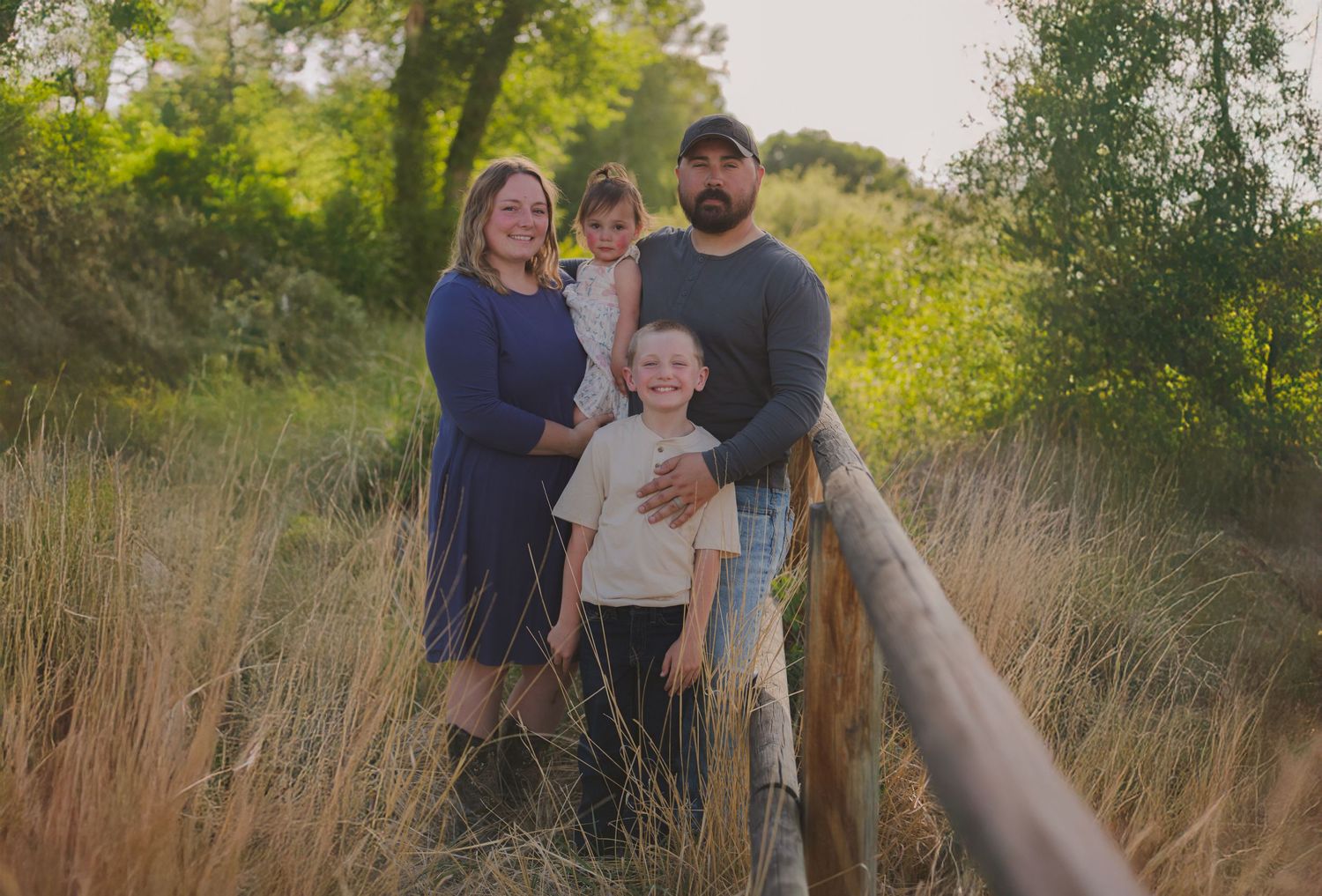 A group stands together on a wooden walkway surrounded by tall grass and trees during golden hour.