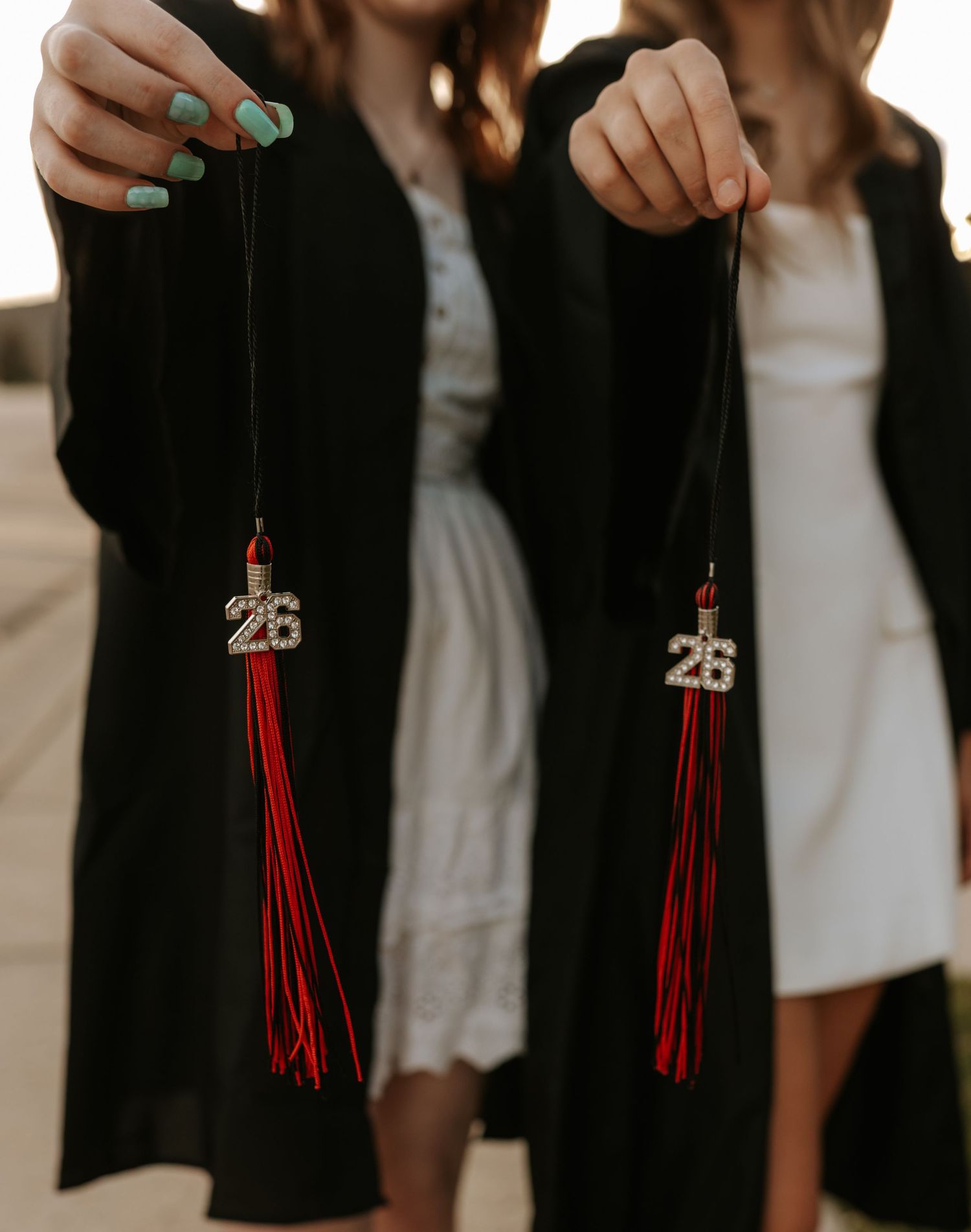 Two graduates in black robes hold red tassel keychains with '26' charms, celebrating their class of 2026 graduation.