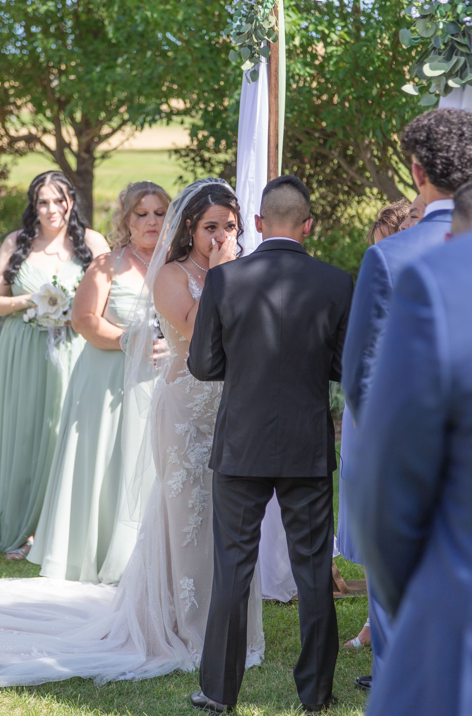 An outdoor wedding ceremony takes place in a garden setting with bridesmaids in mint green dresses standing at the altar.