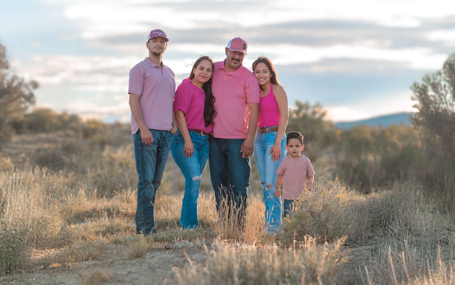 A group of five people wearing pink and blue outfits pose together in a desert landscape at sunset.
