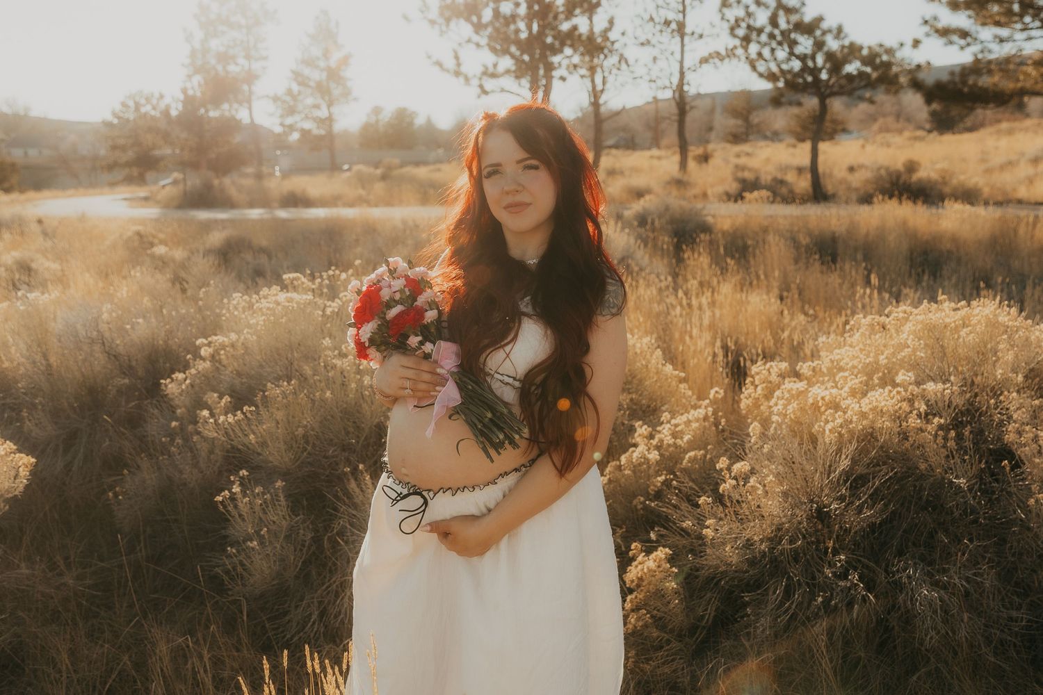 A dreamy golden hour photoshoot in a rustic field with tall grasses and soft sunlight filtering through the trees.