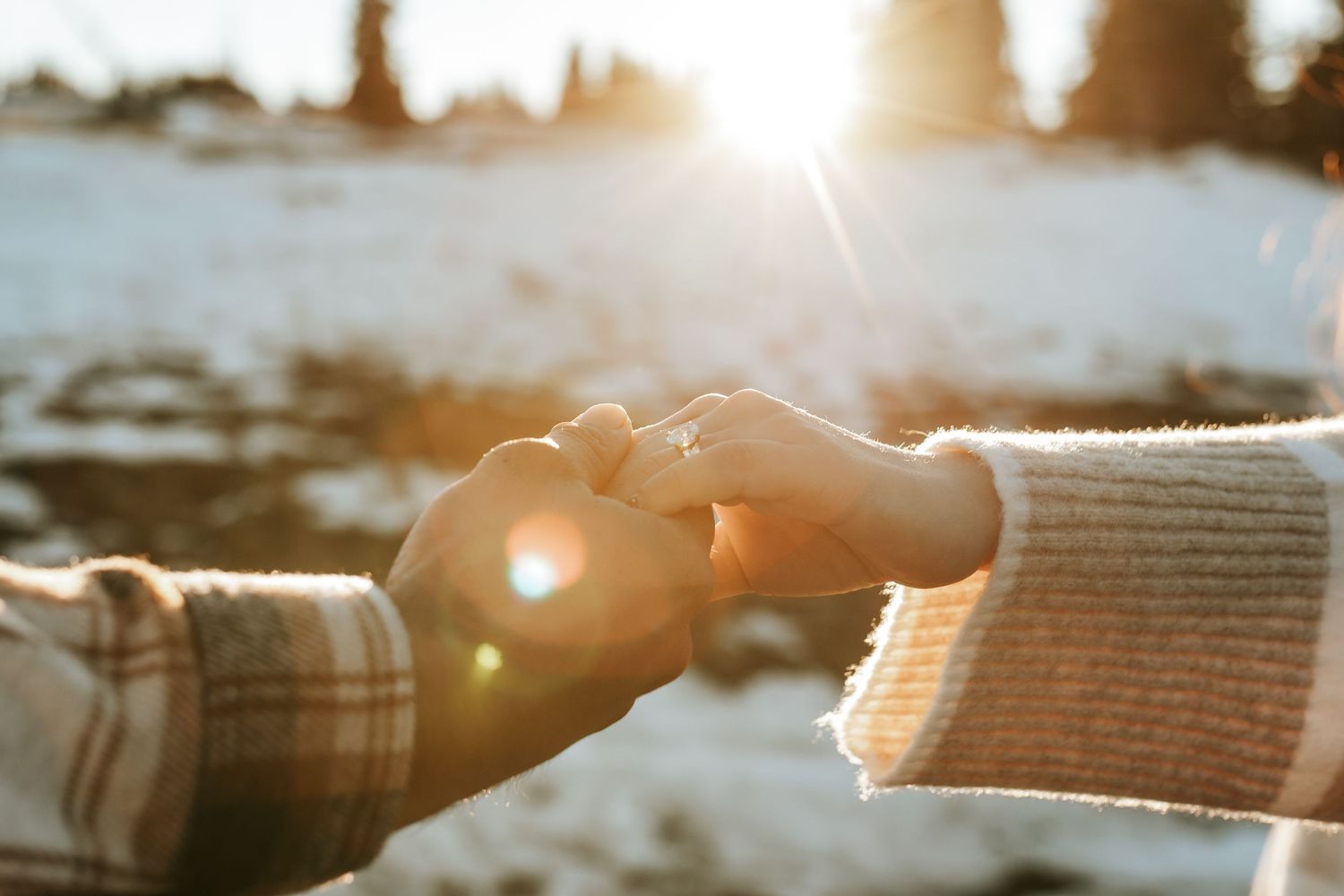 Two hands reaching towards each other against a bright sunlit winter background with snow and lens flare.