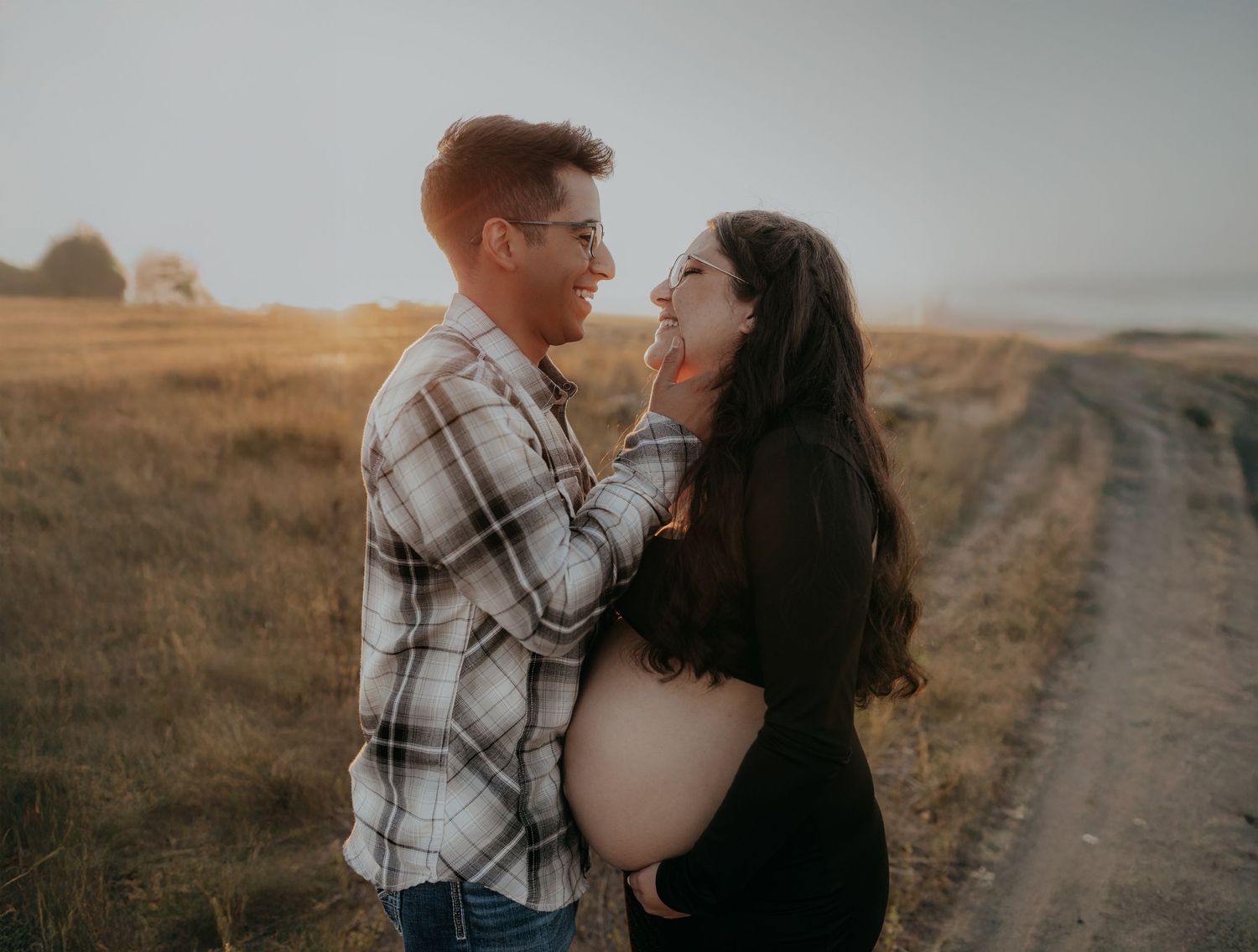 A couple embraces on a dirt road during a sunset maternity photoshoot.