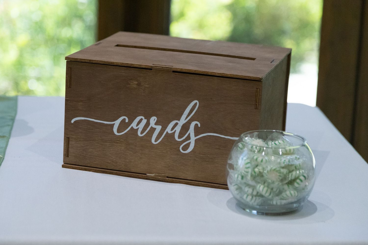 Rustic wooden card box with calligraphy text and small glass vase centerpiece on white tablecloth.
