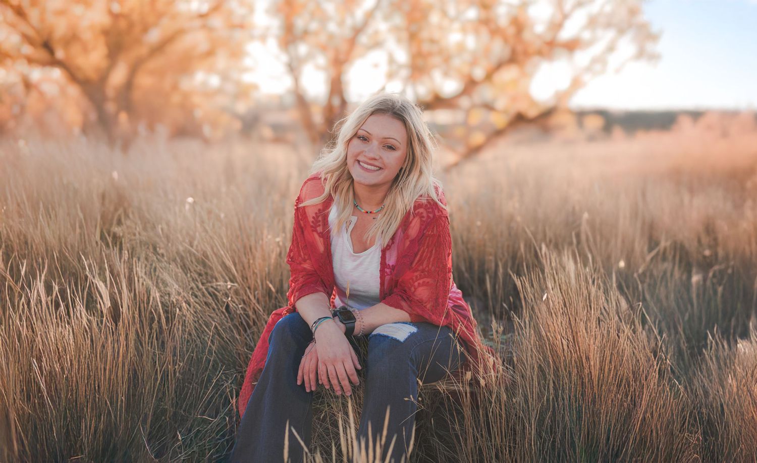 Person in red sweater sitting among tall grass during sunset.