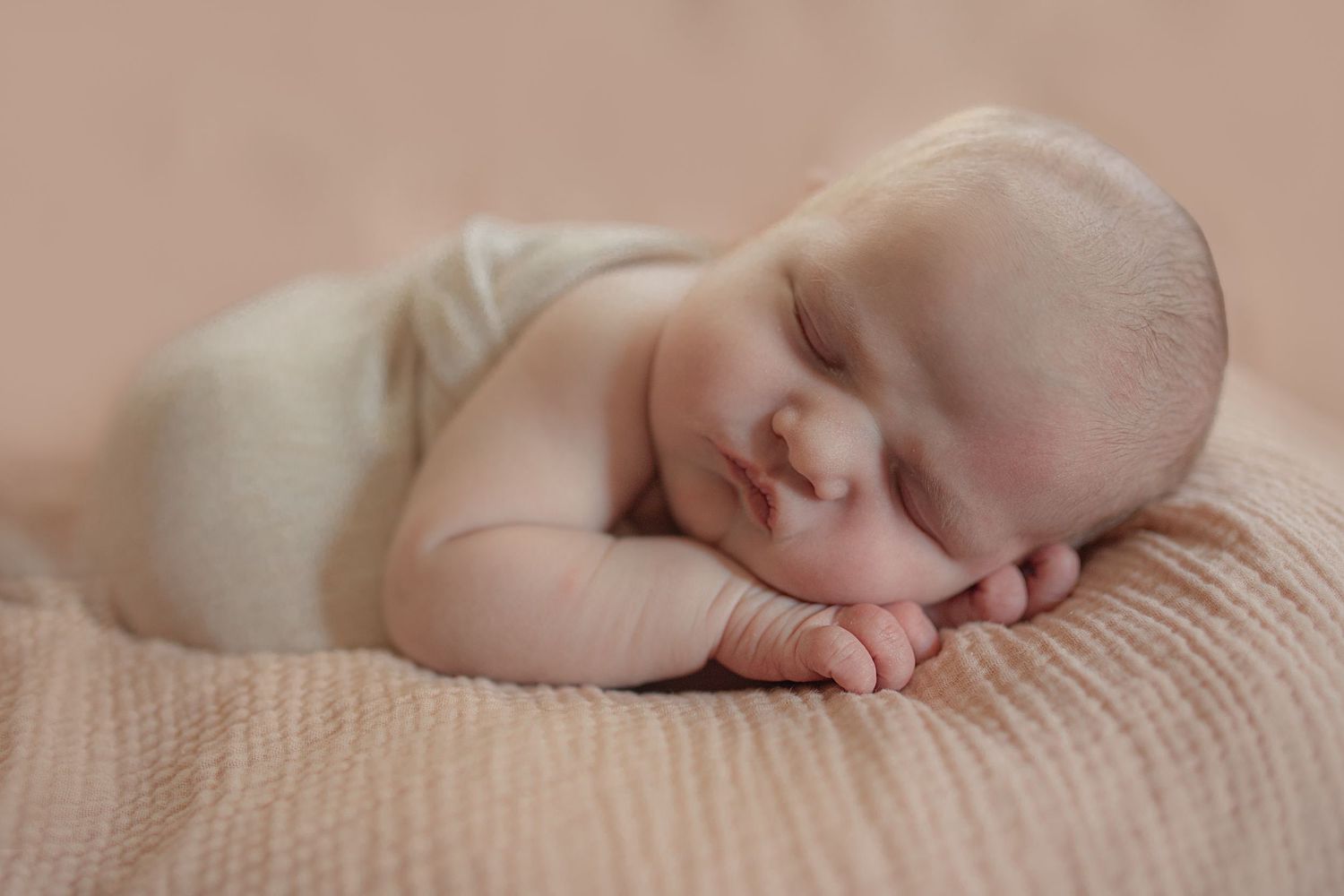 A peaceful sleeping newborn baby wrapped in soft beige fabric.