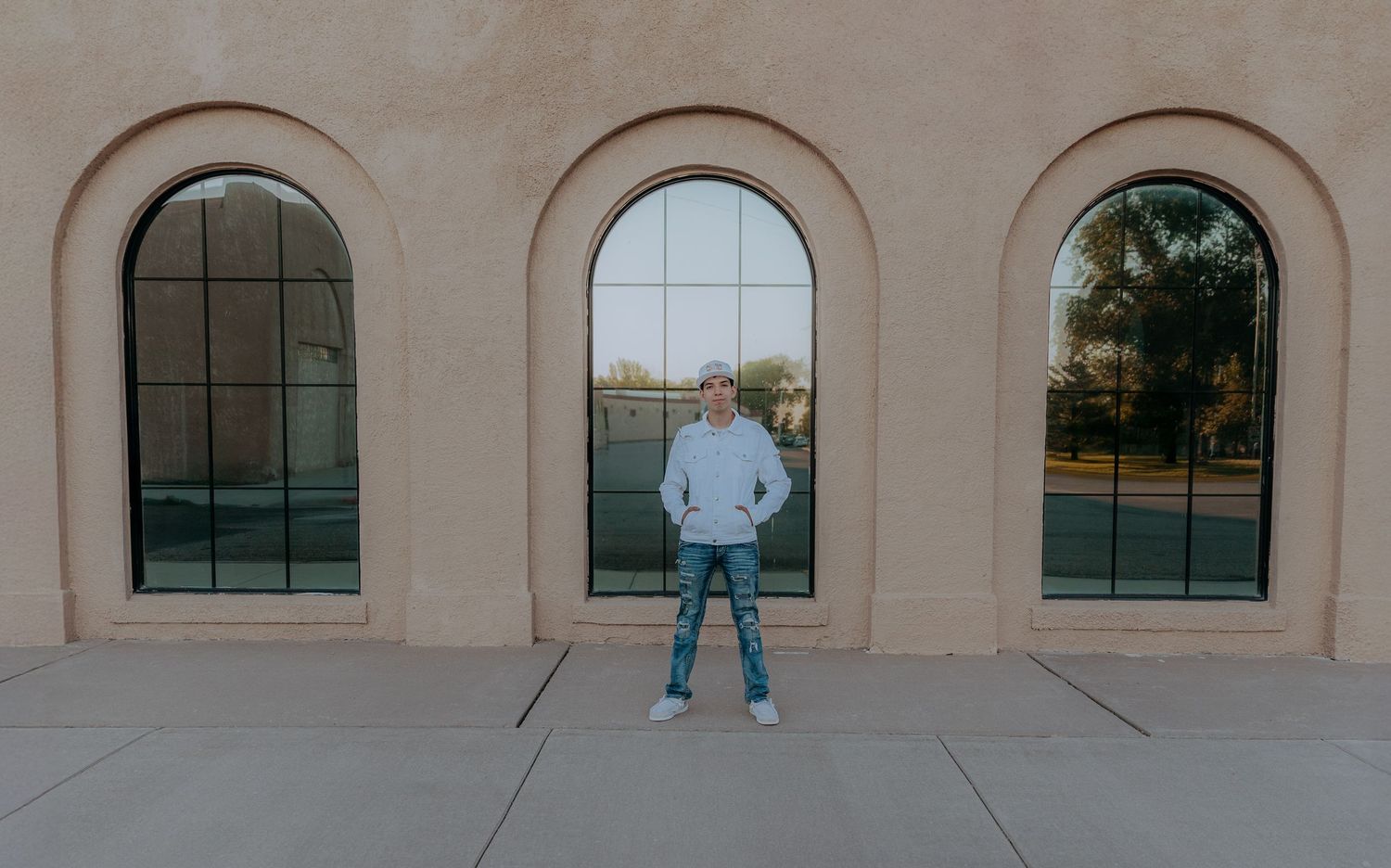Person in gray hoodie standing before arched windows on a tan stucco building exterior.