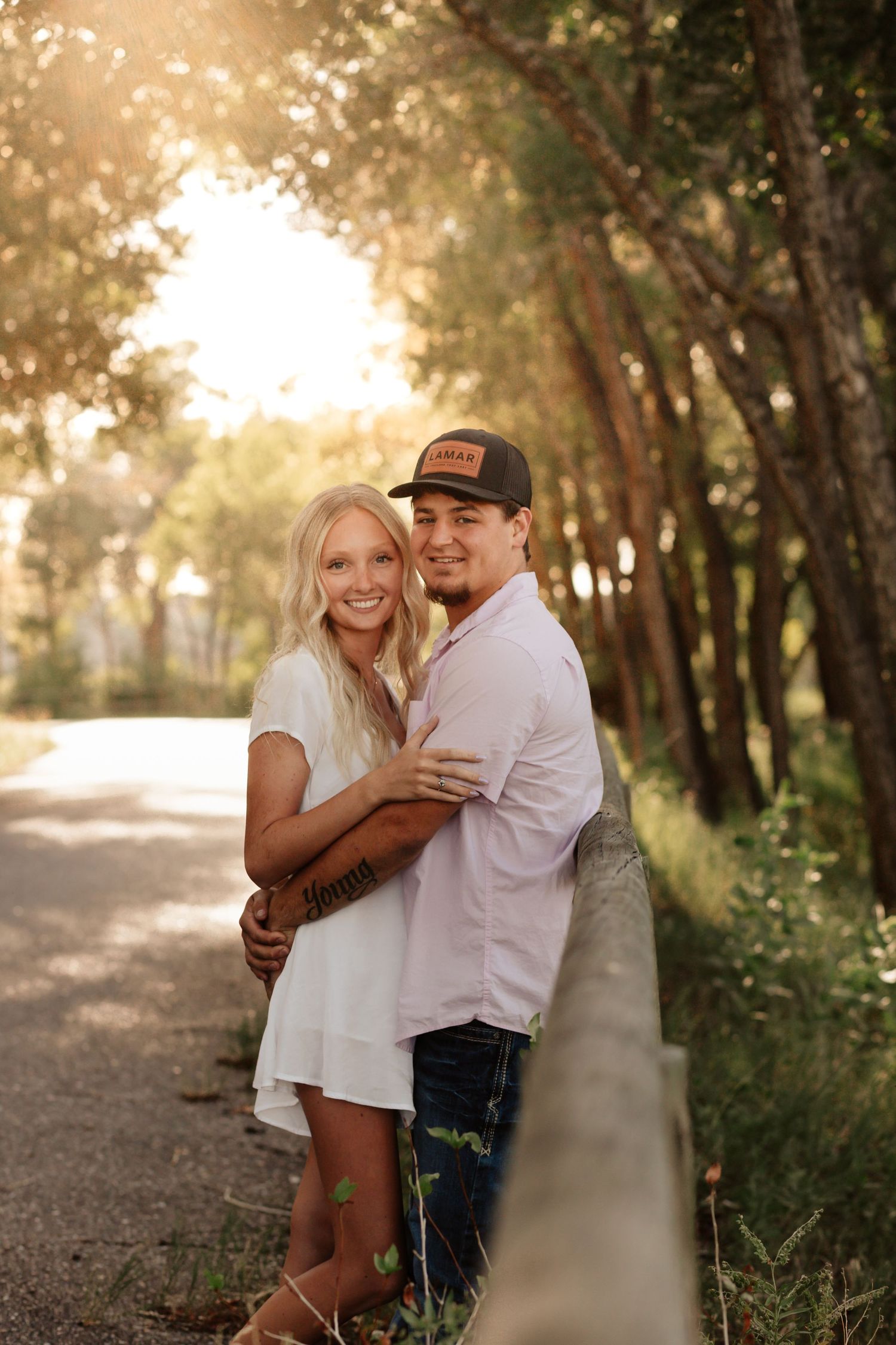 Happy couple embraces on sunlit forest path during golden hour sunset in summer setting.