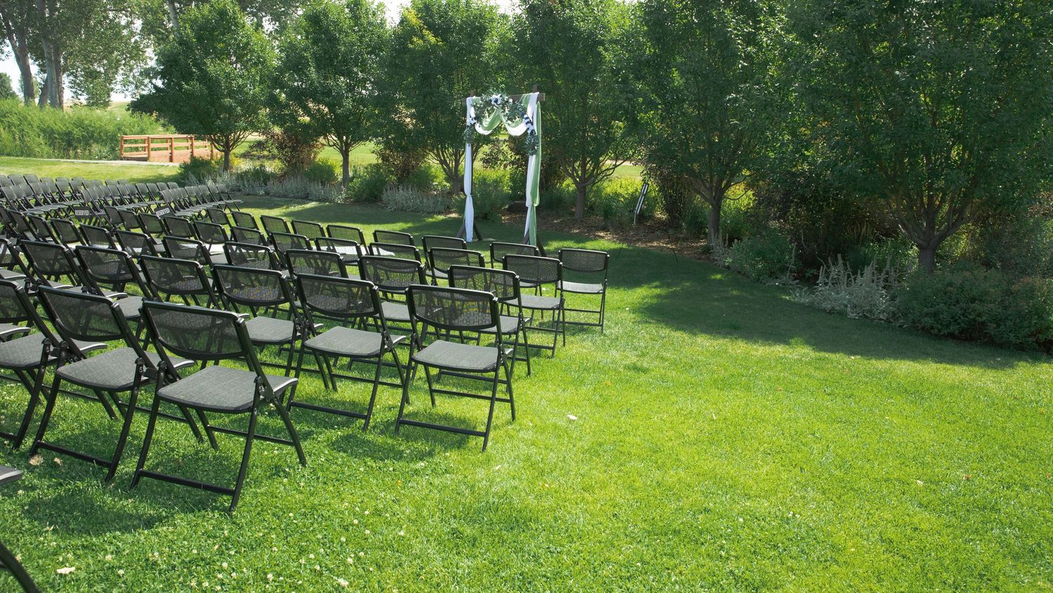 Rows of ornate black metal patio chairs arranged on a lush green lawn at an outdoor event venue.